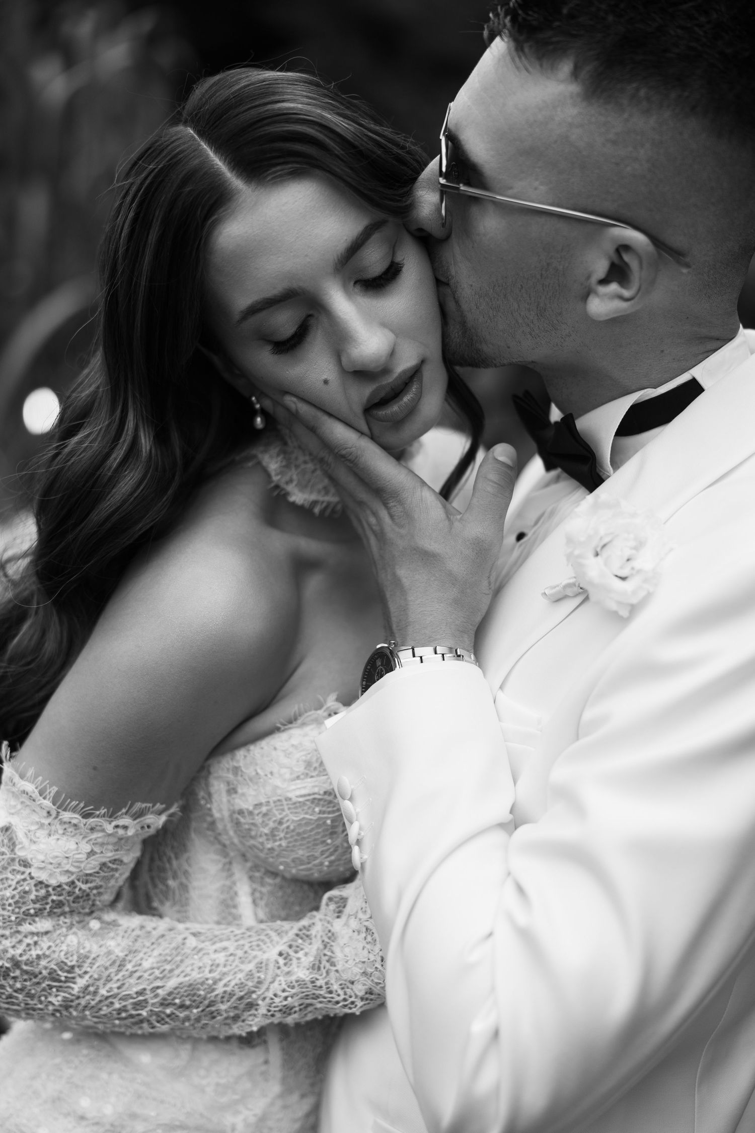 Black and white wedding photo of groom tenderly kissing bride's cheek while cradling her face.