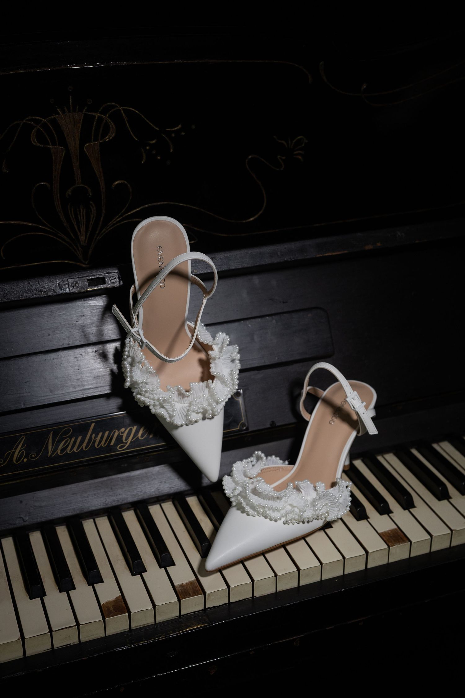 White pearl-embellished bridal heels with ankle straps displayed on vintage A. Neuburger piano keys.