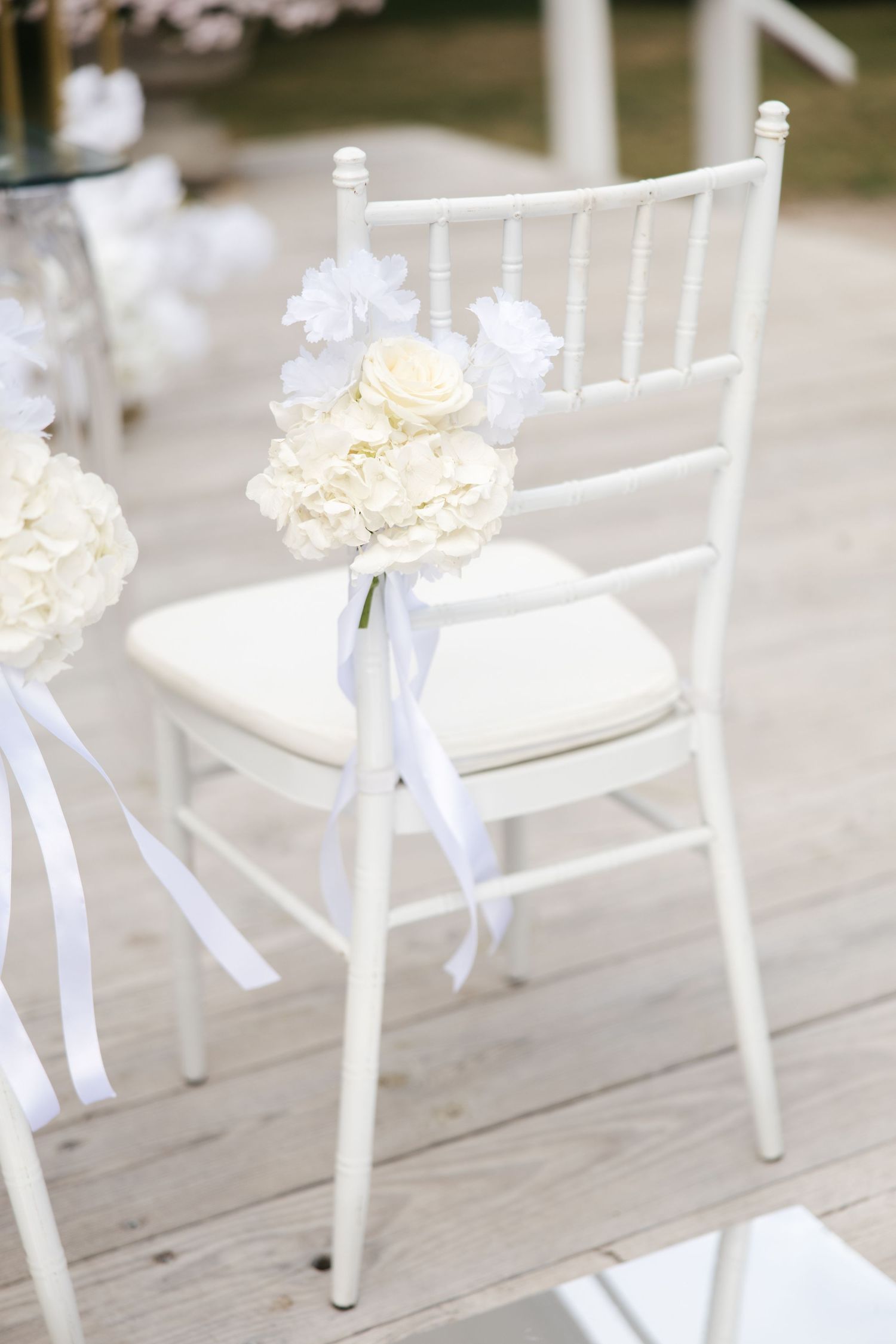 White Chiavari chair decorated with ivory roses, hydrangeas, and white ribbon bow for an elegant wedding ceremony.