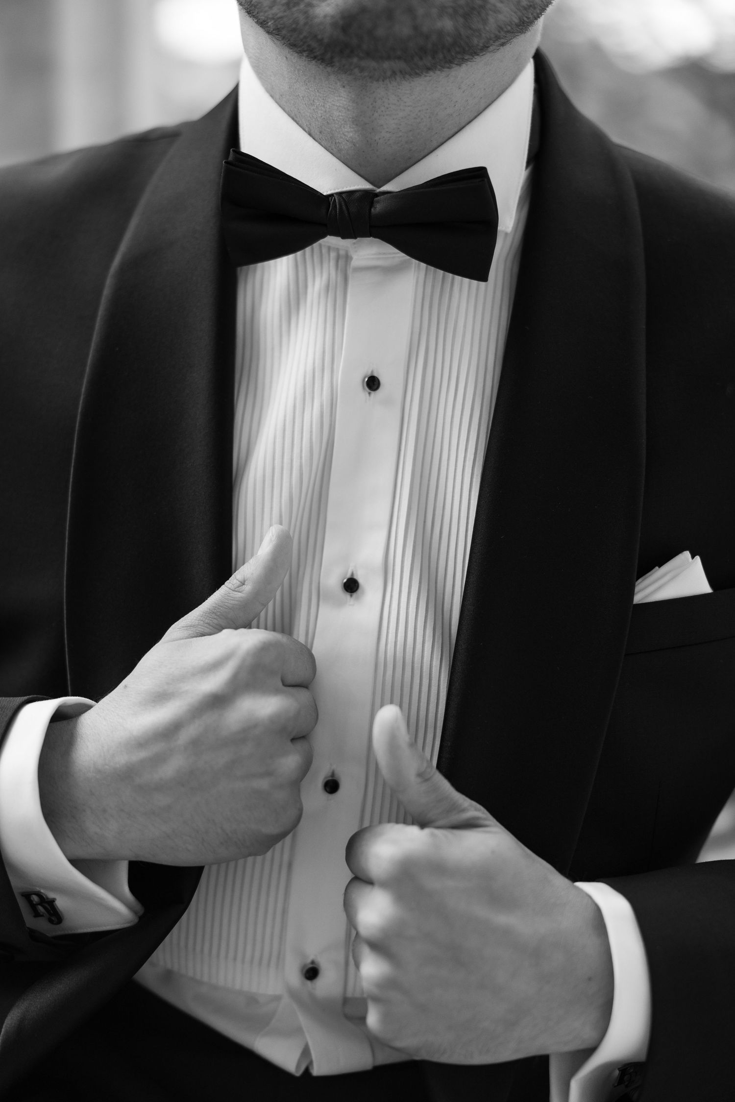 Black and white photo of a groom in a tuxedo with bow tie adjusting his jacket lapels.