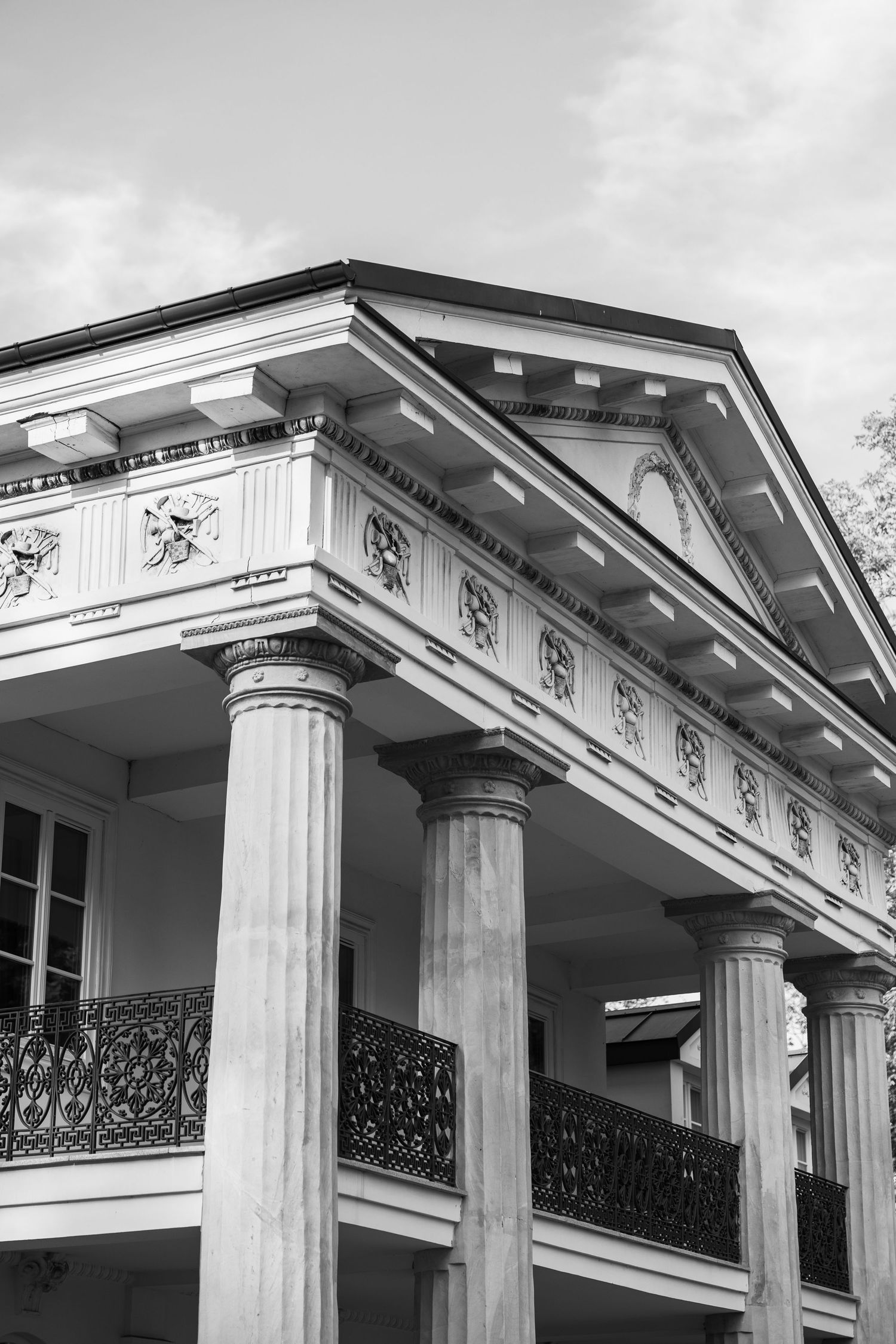 Black and white photo of a grand neoclassical building with tall columns, ornate friezes, and decorative iron railings.