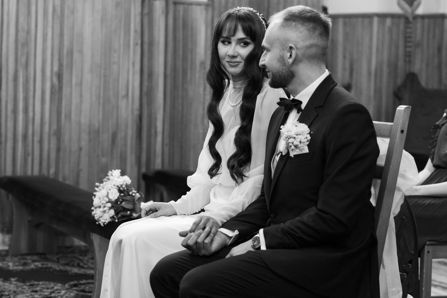 A black and white wedding photo shows a couple seated together during their ceremony in formal attire.