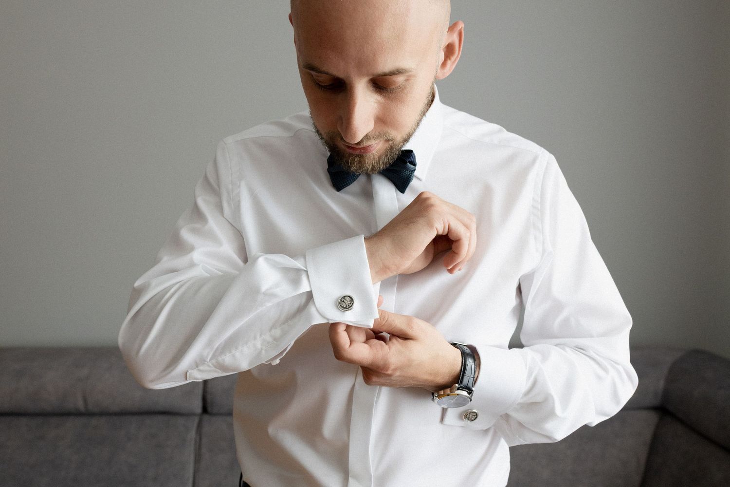 A person in a crisp white dress shirt adjusts their cuff while wearing a black bowtie and wristwatch.