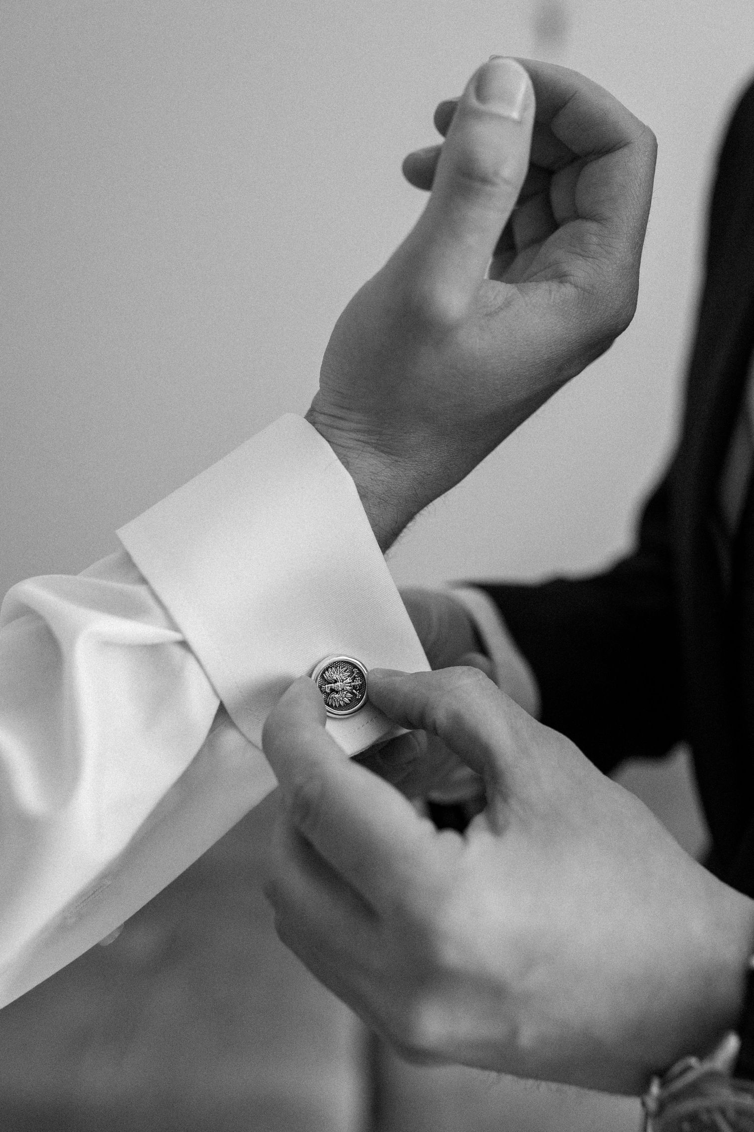 Black and white close-up of hands adjusting a formal white shirt cuff with cufflinks.