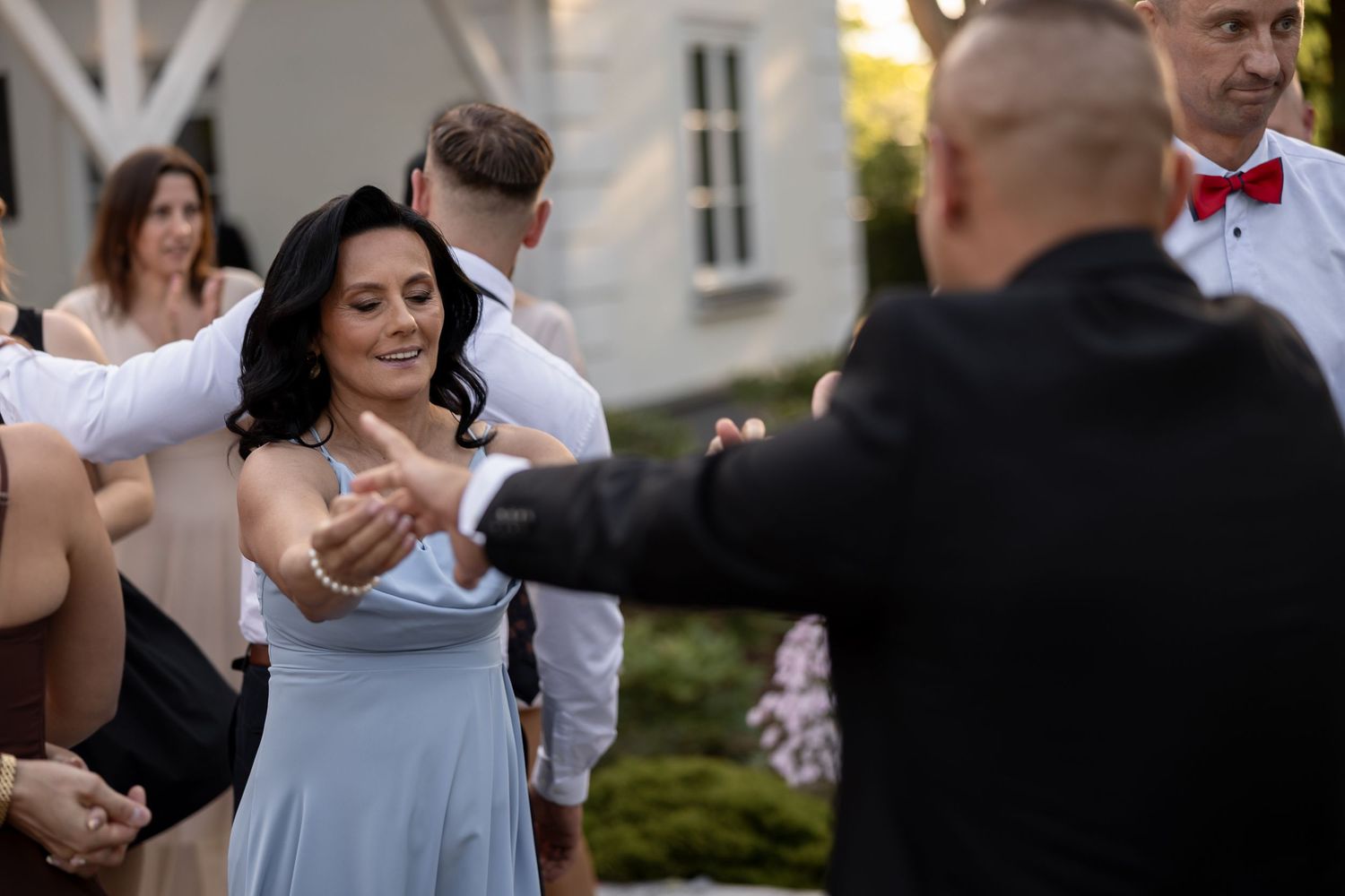 A woman in a light blue dress dances outdoors at a wedding reception with guests gathered around her.