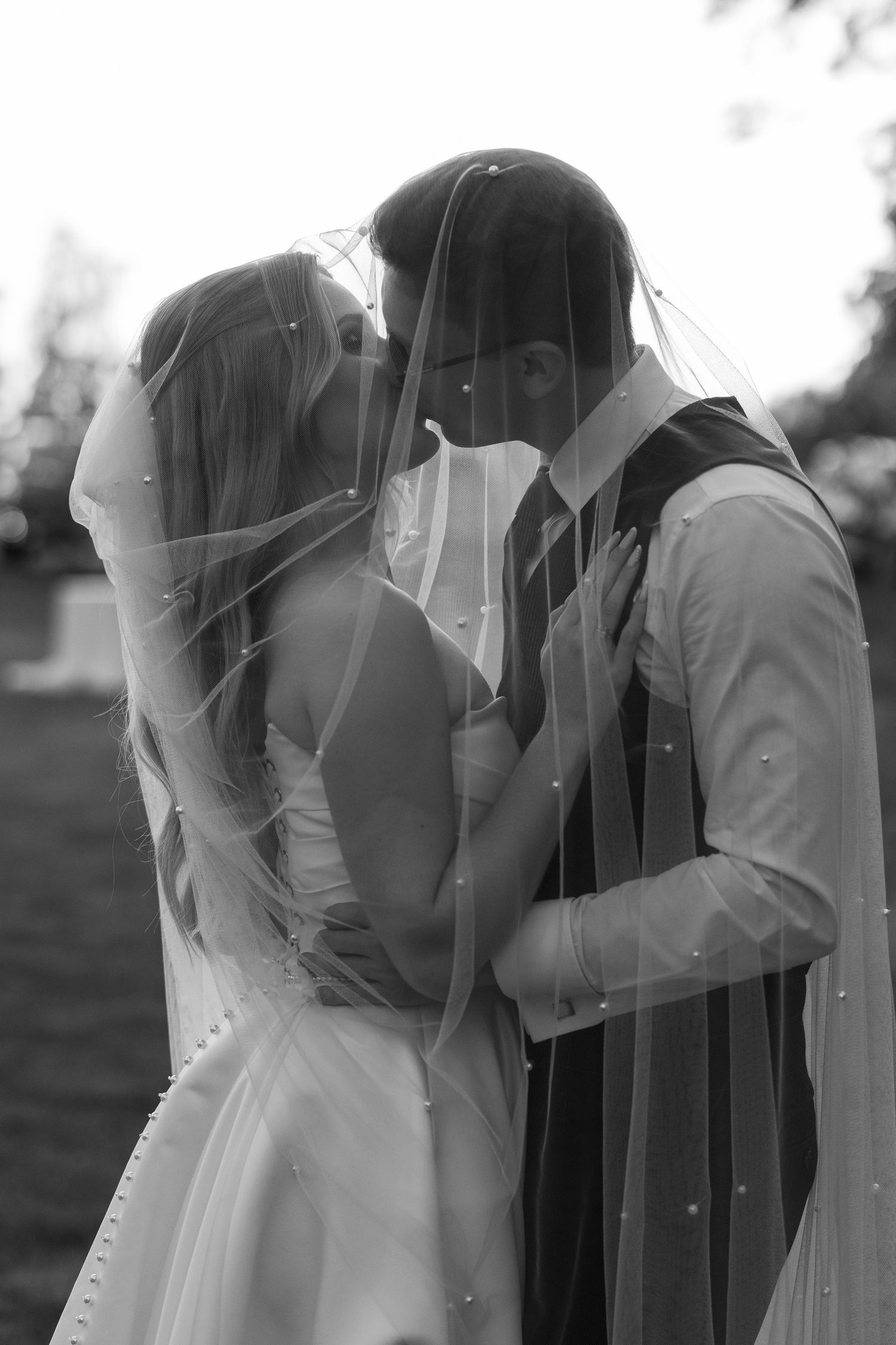 A romantic black and white wedding photograph showing a tender kiss between newlyweds under a delicate veil.
