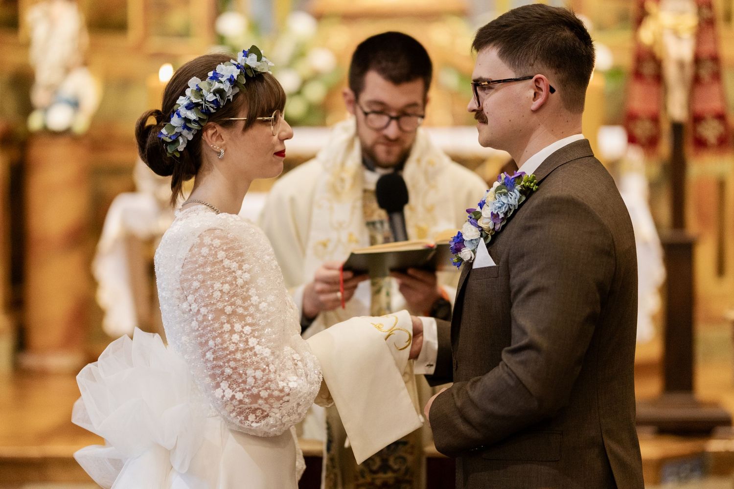 Couple exchanges vows during wedding ceremony inside ornate church with officiant leading traditional service.