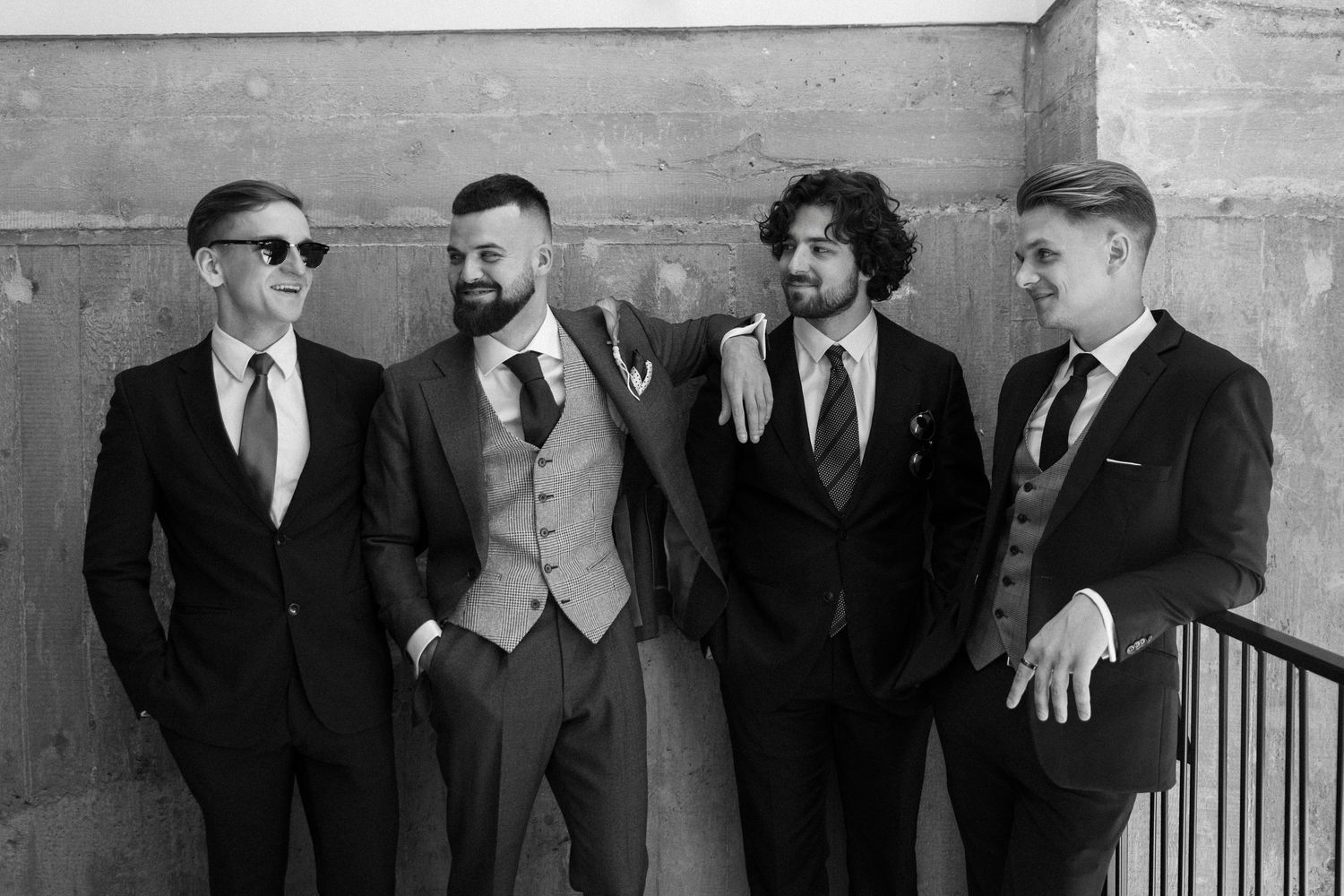 A black and white photo of four men in formal attire standing together against a wall.