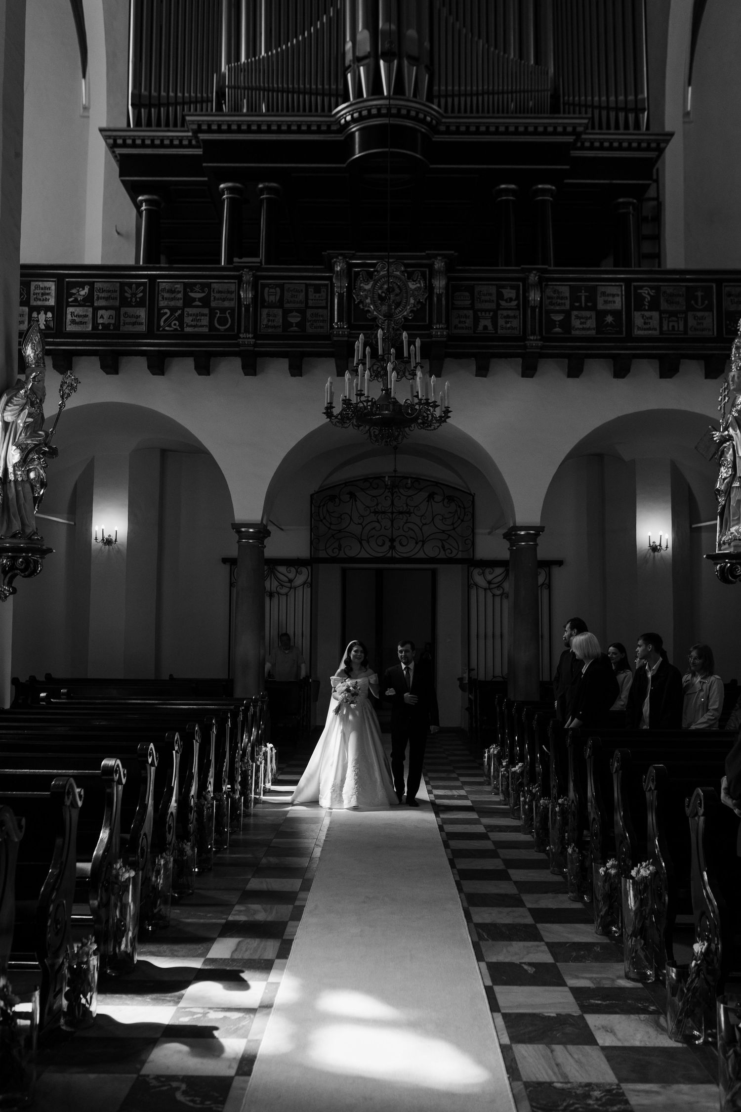 A dramatic black and white photo of a wedding ceremony in a church with a white aisle runner and pipe organ in the background.