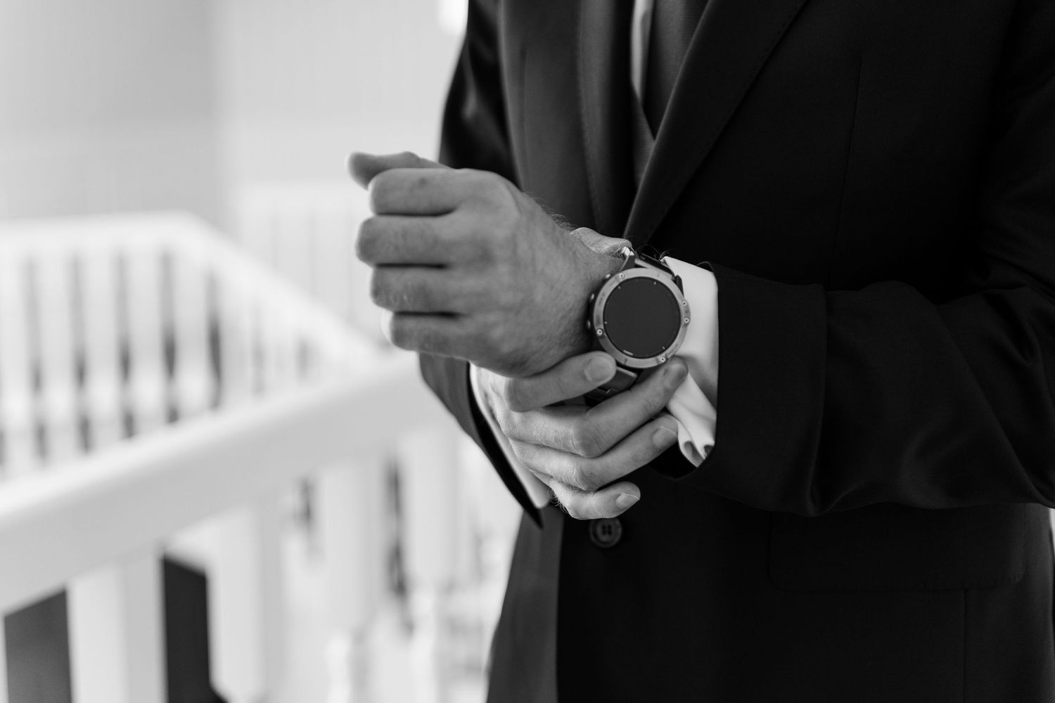 Black and white photo showing hands adjusting a wristwatch while wearing formal business attire.