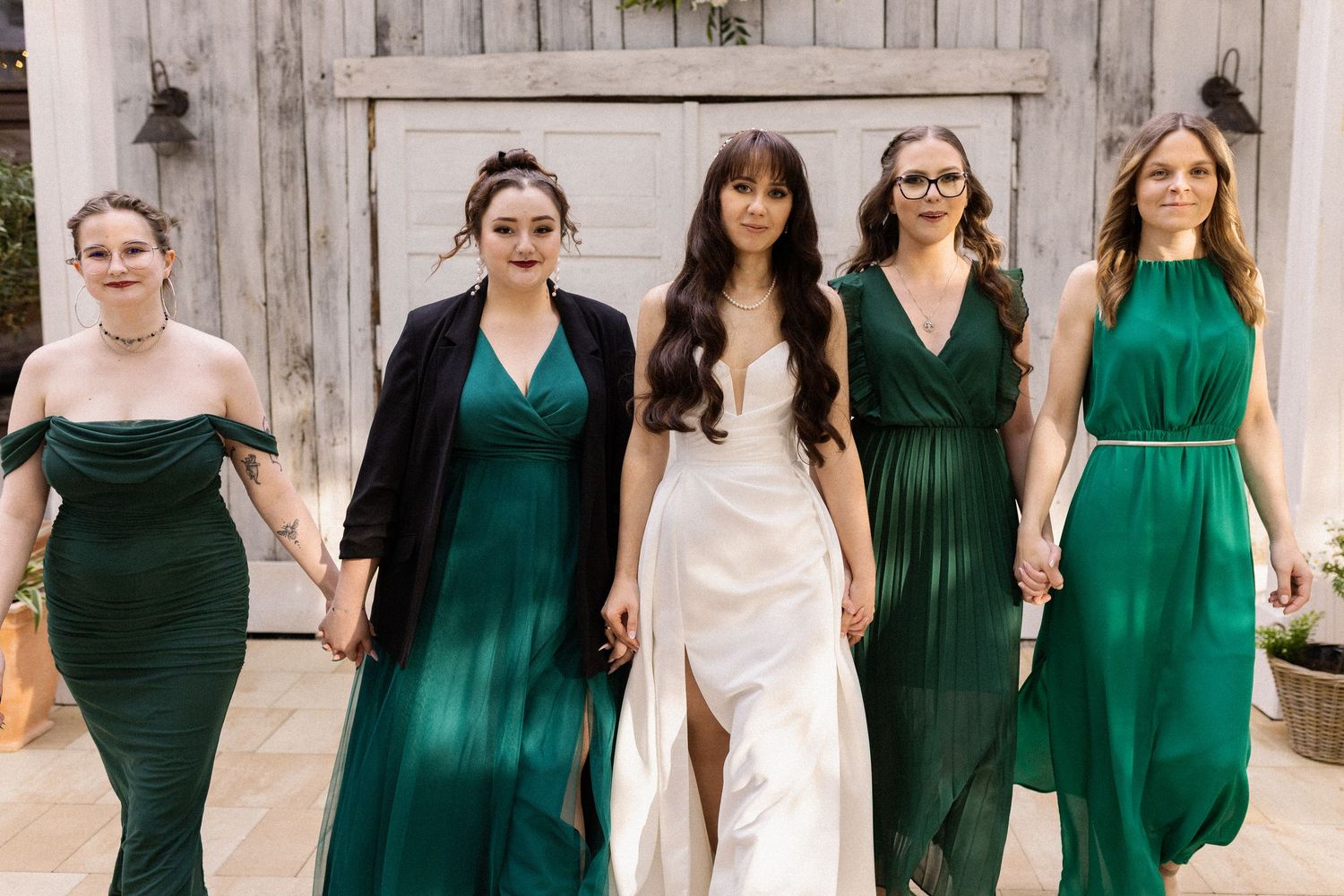 Wedding party poses together with bride in white dress and attendants wearing coordinating emerald green dresses.