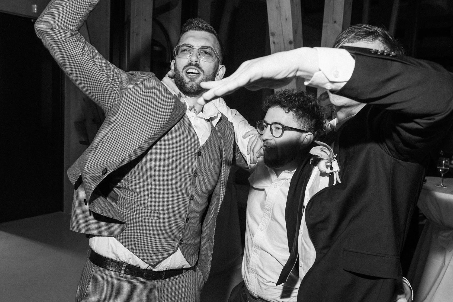 Group of wedding guests dancing joyfully at a reception in black and white photography.
