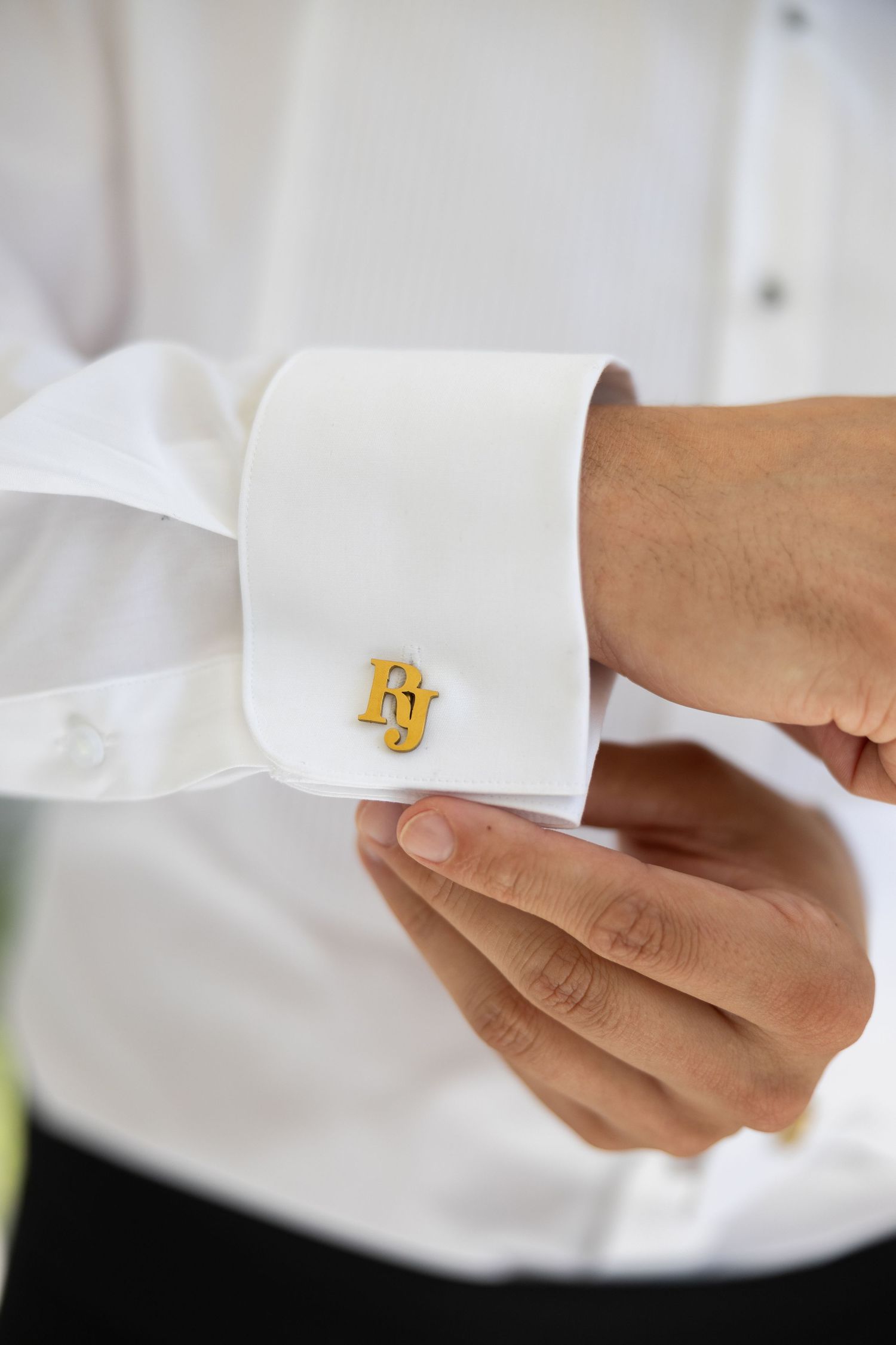 Man in white dress shirt adjusting gold monogram FJ cufflinks on his sleeve.