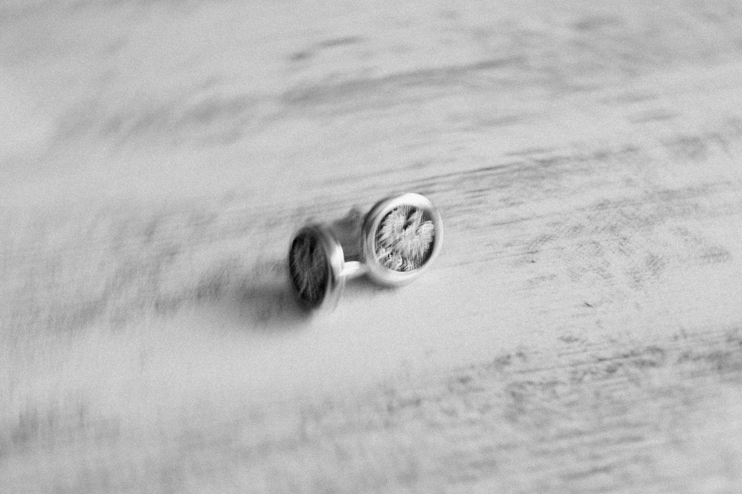 A black and white motion-blurred photograph of a Volkswagen logo hubcap in motion on a textured surface.