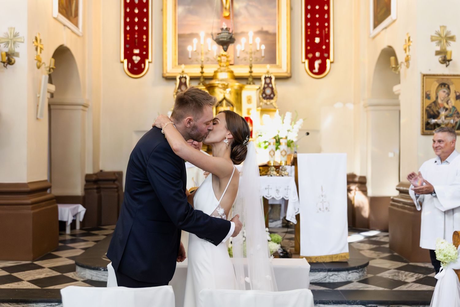 A couple shares their first kiss as newlyweds at the altar of an ornate Catholic church during their wedding ceremony.