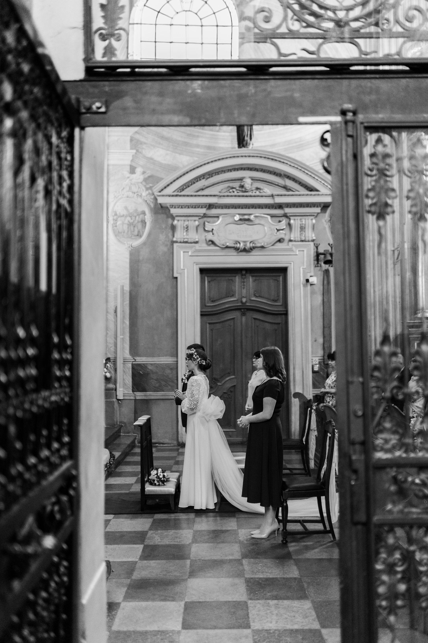 A black and white vintage photograph showing two figures standing in an elegant hallway with checkered floors and ornate decor.