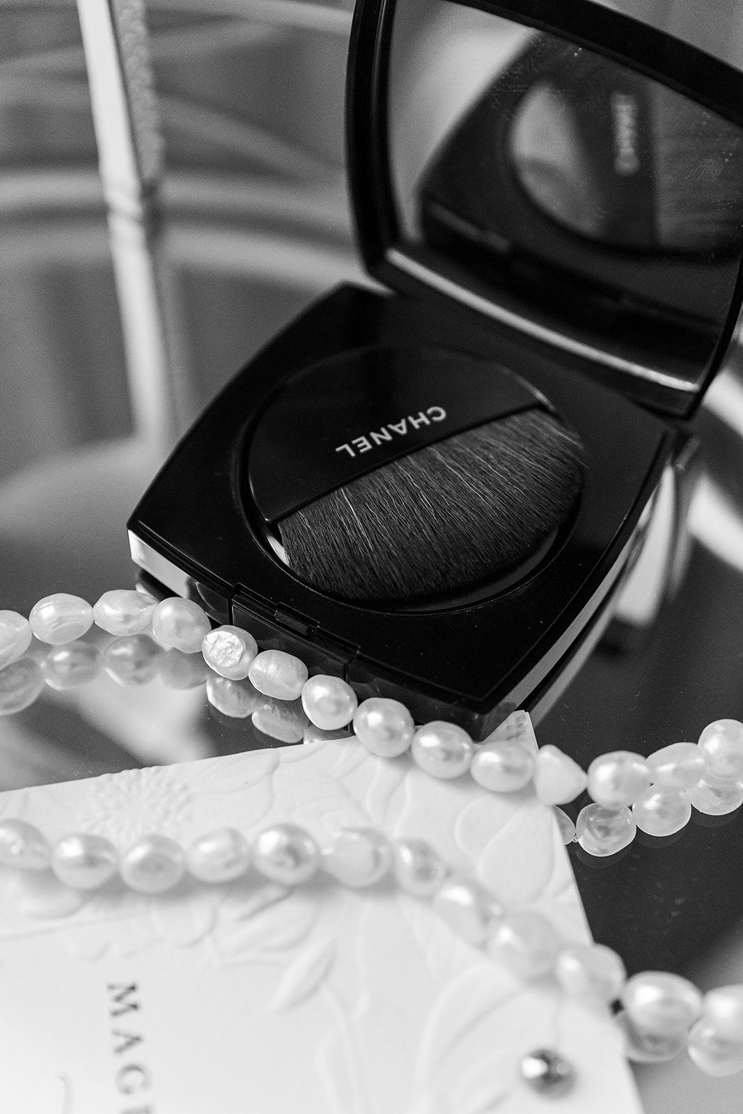 A strand of white pearls elegantly draped beside a black compact makeup case on a white surface.