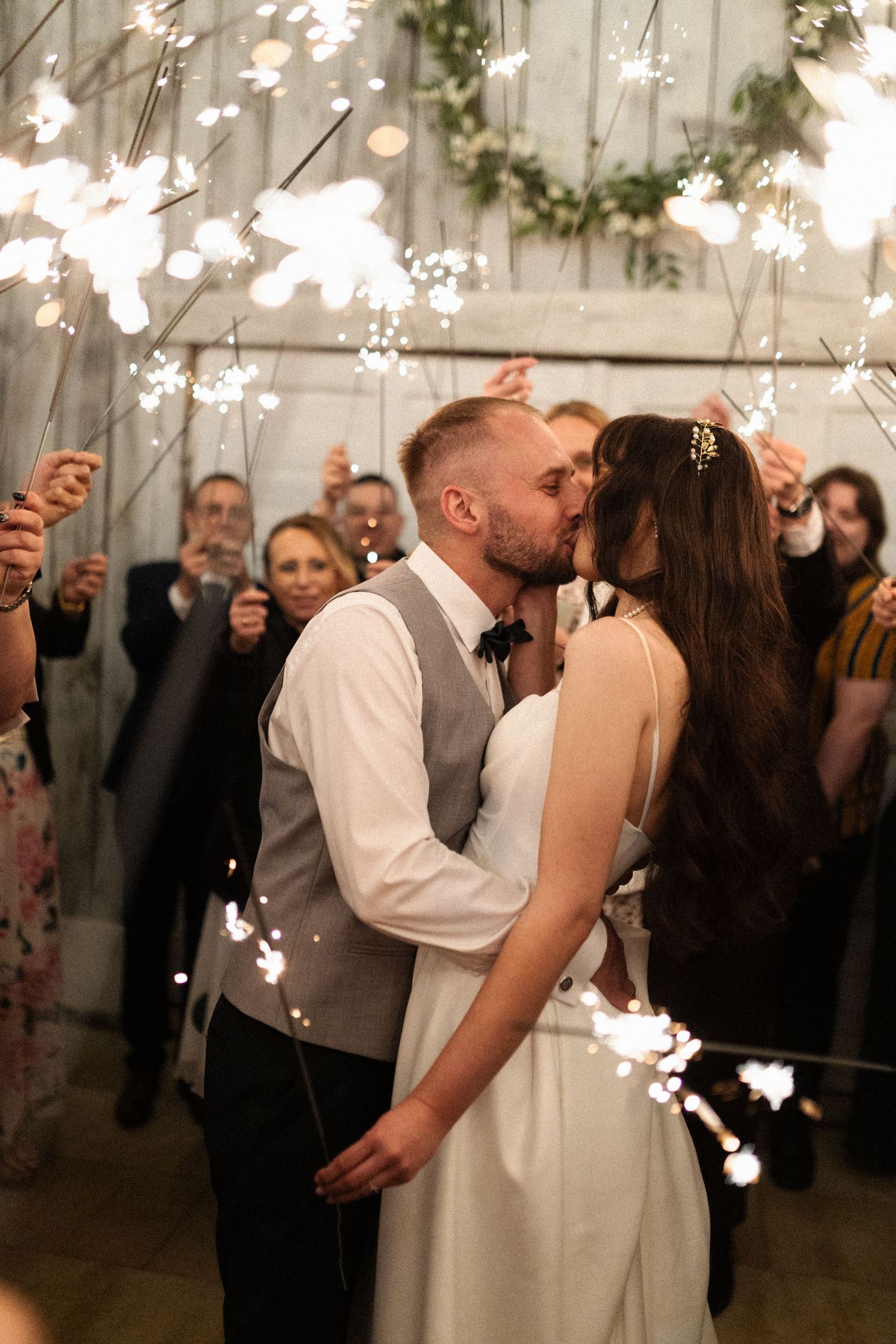 A romantic wedding kiss captured with sparklers and twinkle lights creating a magical atmosphere at an indoor venue.