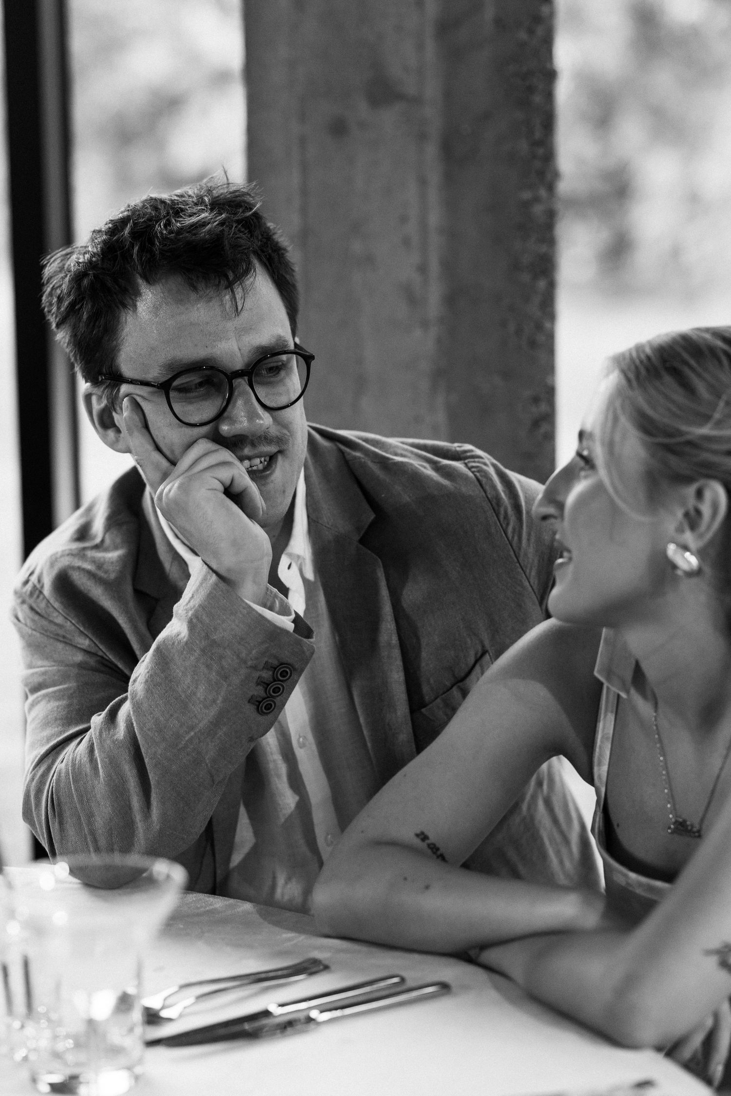 A romantic black and white candid photo of a couple sharing an intimate moment at a restaurant table.