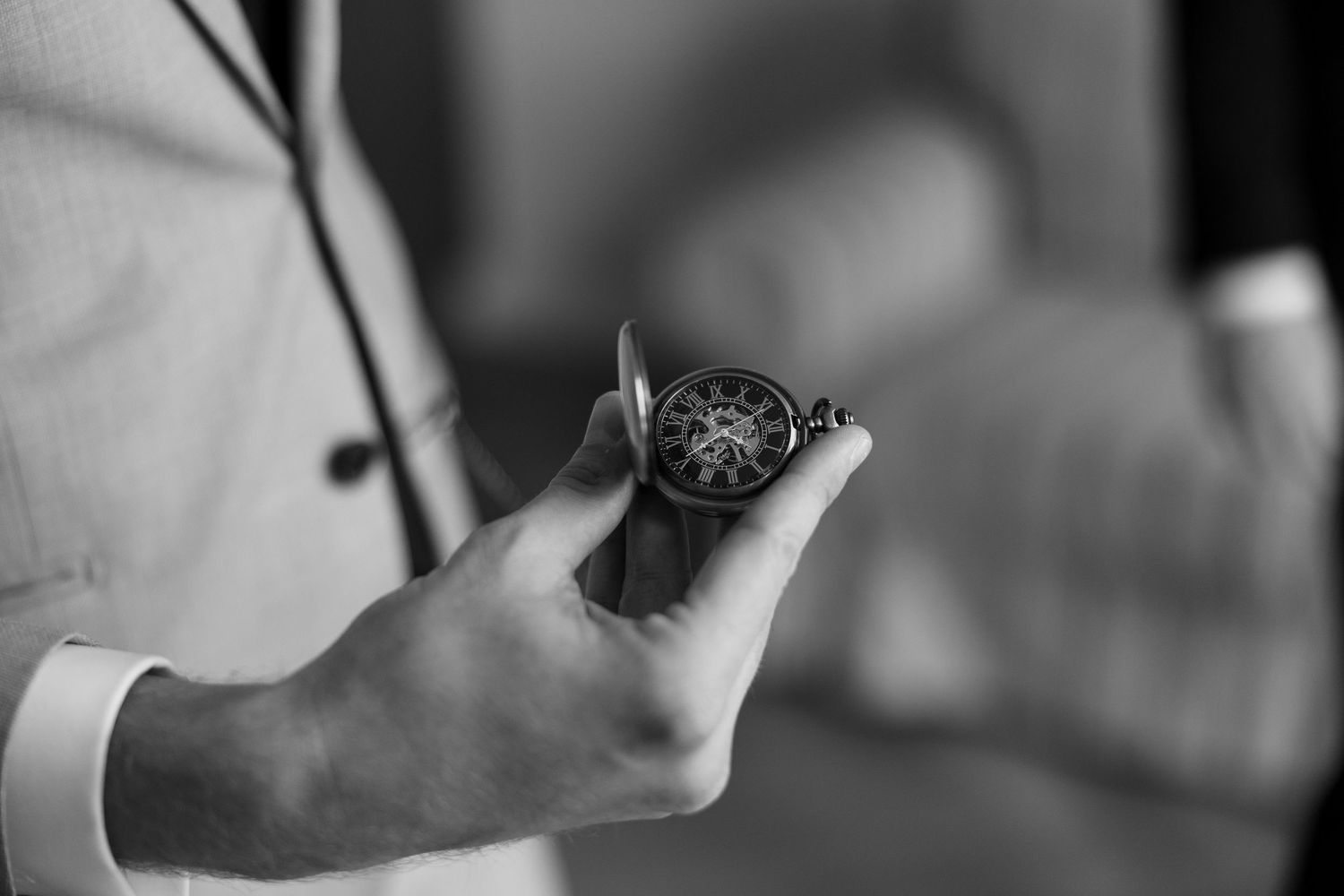 Black and white photo of a man in a suit holding an ornate vintage pocket watch.