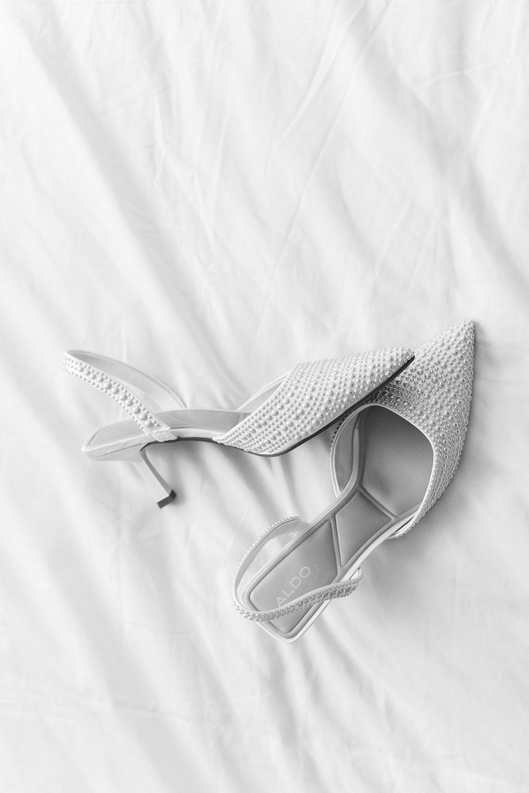 A pair of elegant white lace stiletto heels positioned on a white textured background.