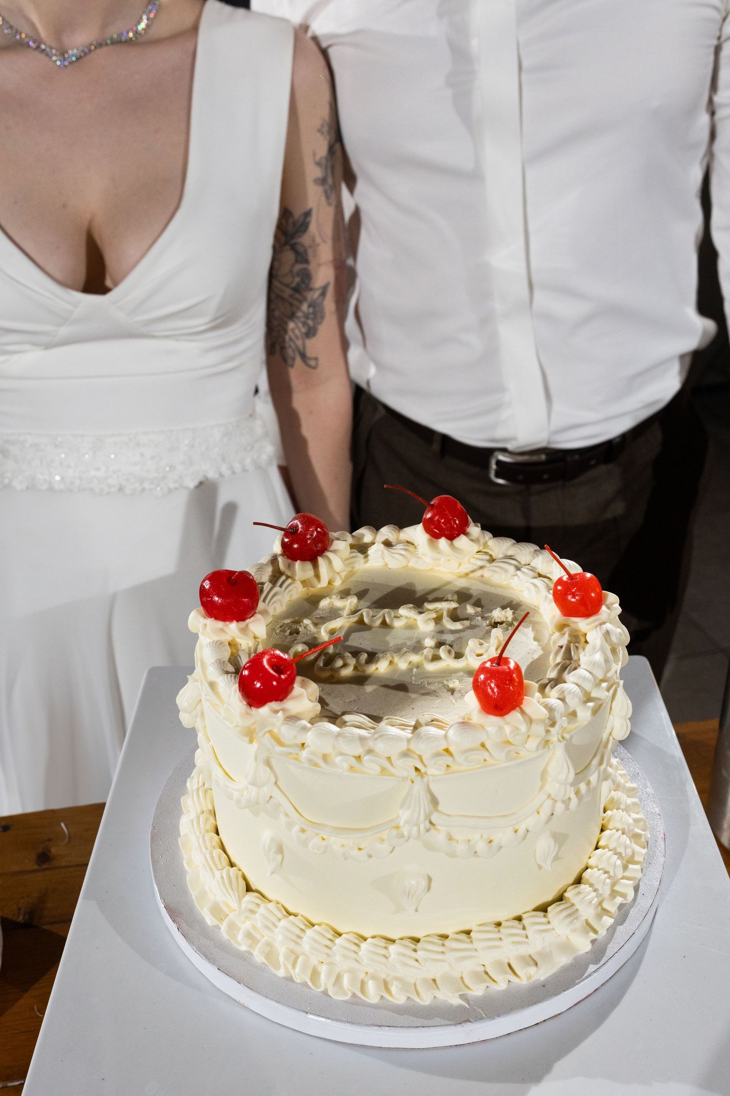 A white wedding cake decorated with buttercream frosting, delicate piping details and bright red maraschino cherries on top.