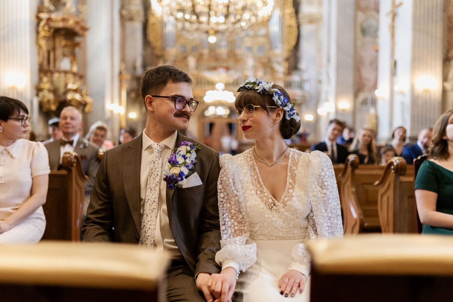 Beautiful couple shares a loving moment during their wedding ceremony inside an ornate church with crystal chandeliers.
