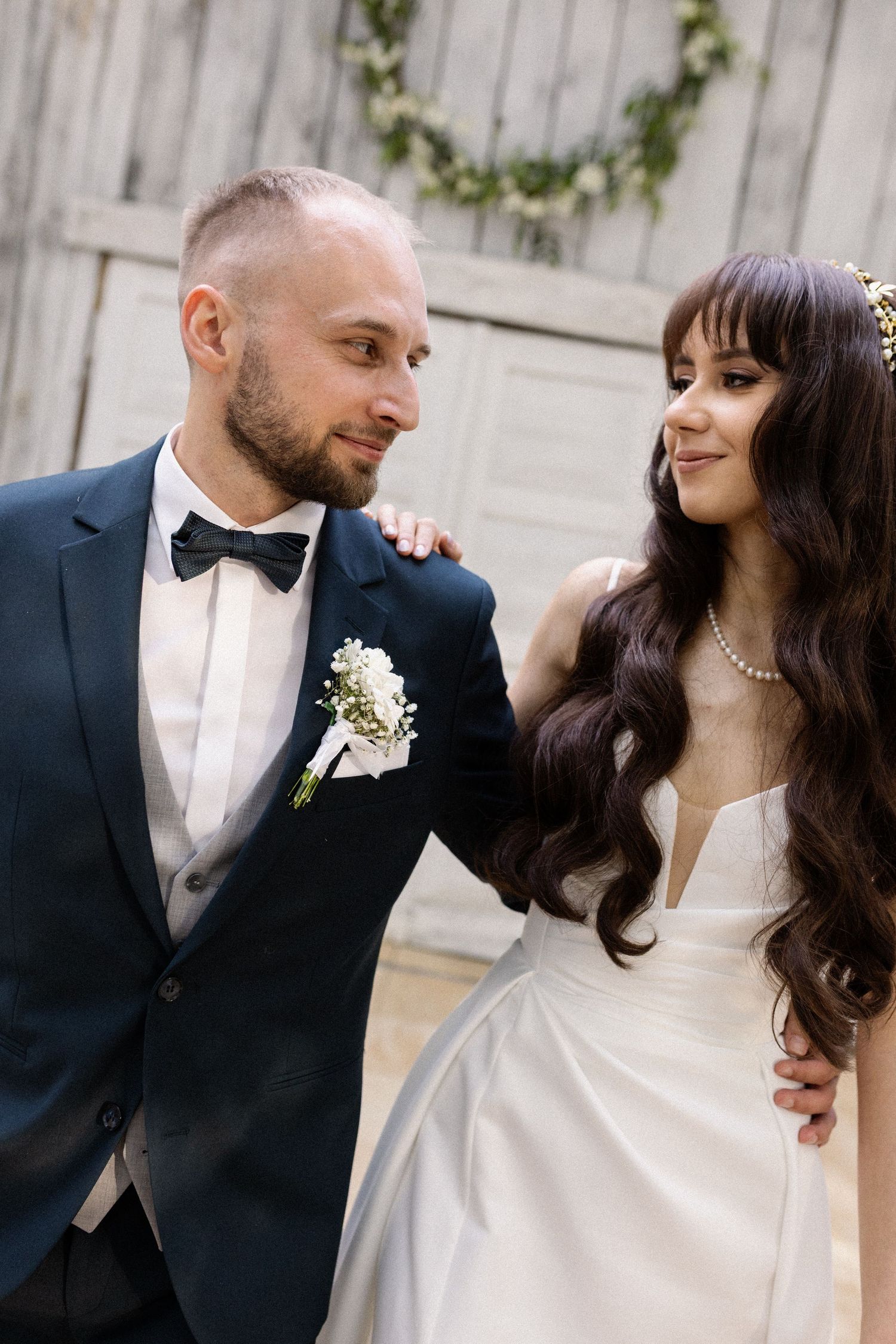 A bride and groom share a sweet moment together at their wedding, with a decorated wooden fence in the background.