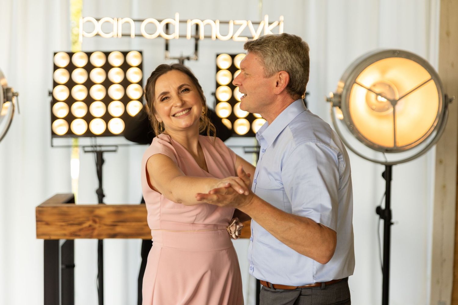 A couple dances together in an elegant room with illuminated circular wall decorations and warm lighting.