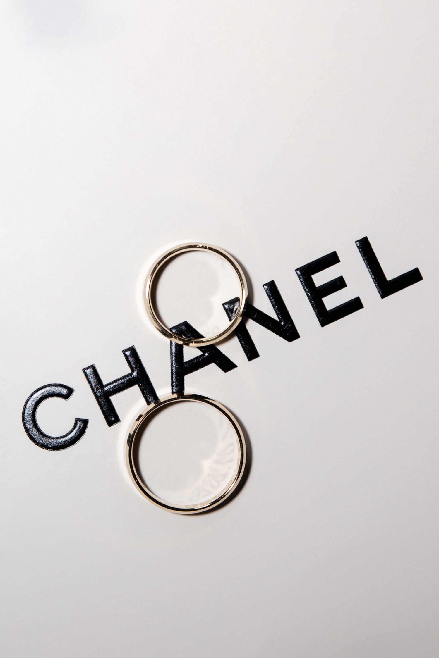 Gold hoop earrings resting on a white surface with black Chanel logo letters spelling the brand name.