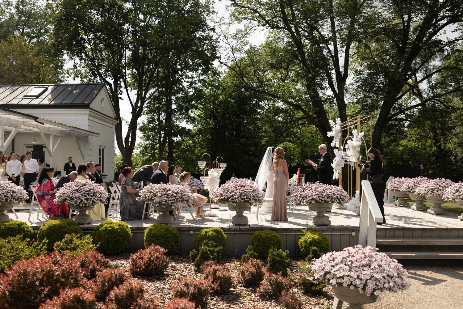 Elegant outdoor wedding ceremony with floral arrangements, bride and groom, and guests in a lush garden setting.