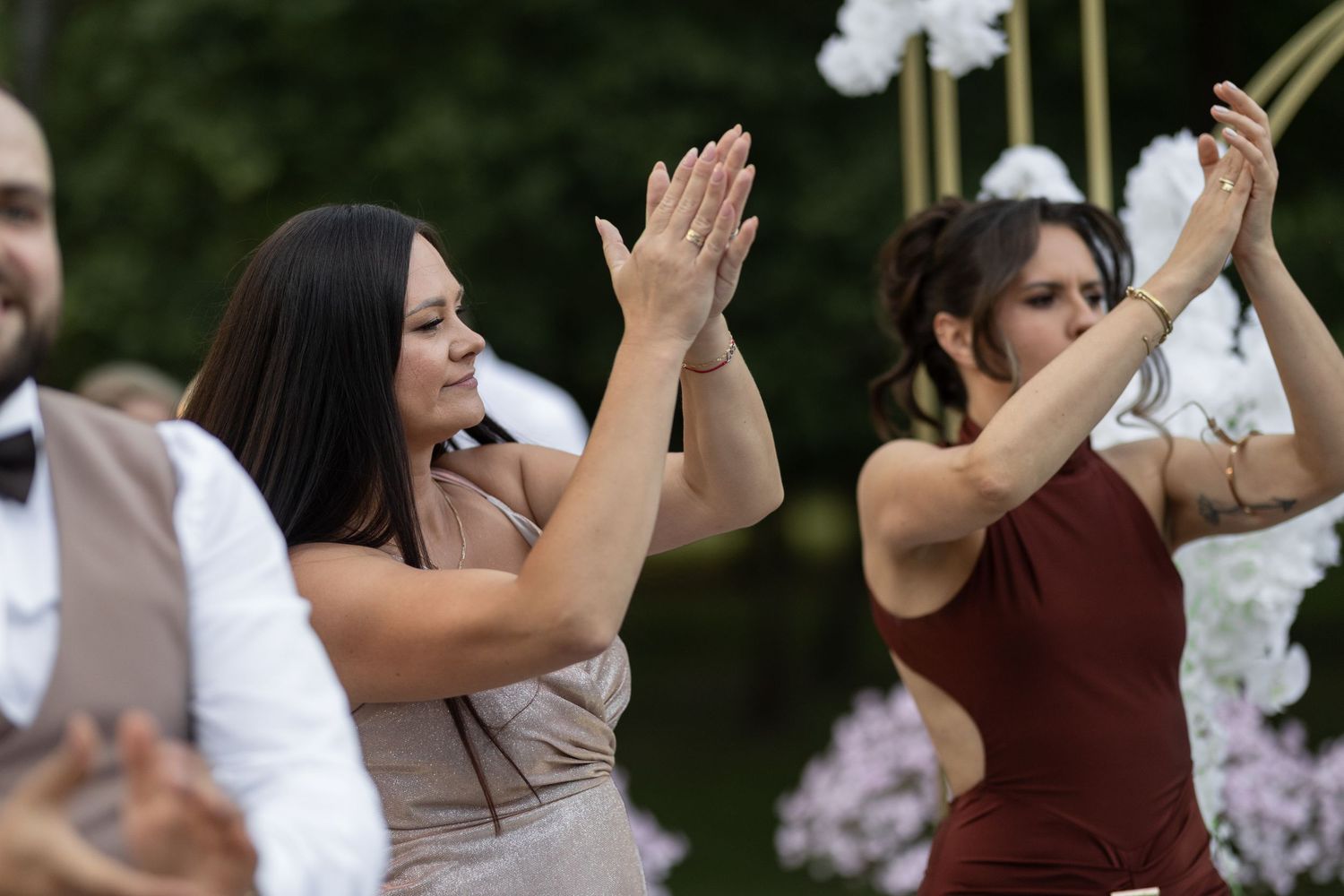 Women dancing outdoors at a wedding reception, raising their arms gracefully near floral decorations.
