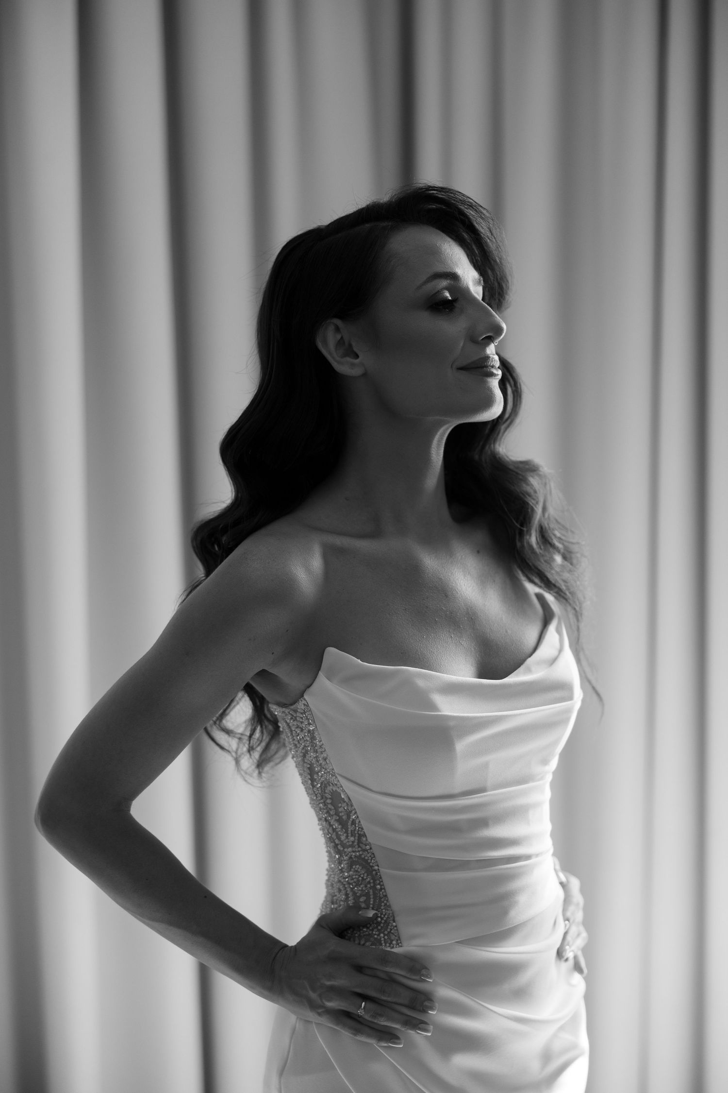 Black and white portrait of a bride in a strapless wedding gown with beaded detail, posing confidently indoors.