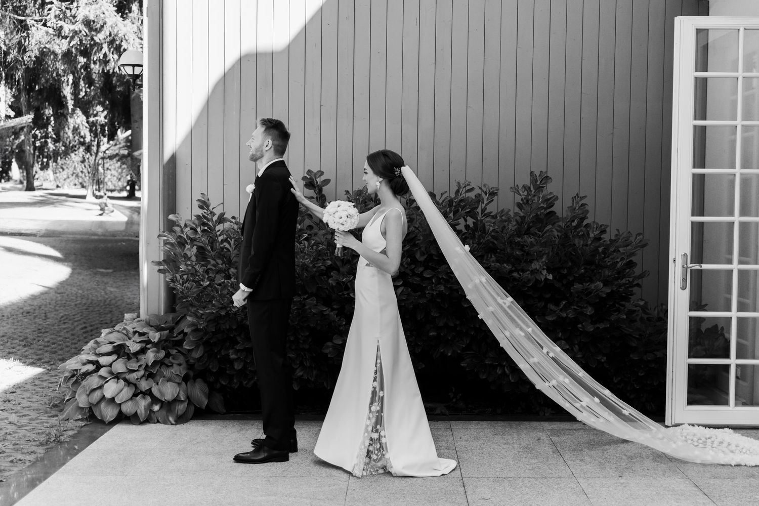 Black and white wedding photograph showing a couple standing facing away from each other outside a building.