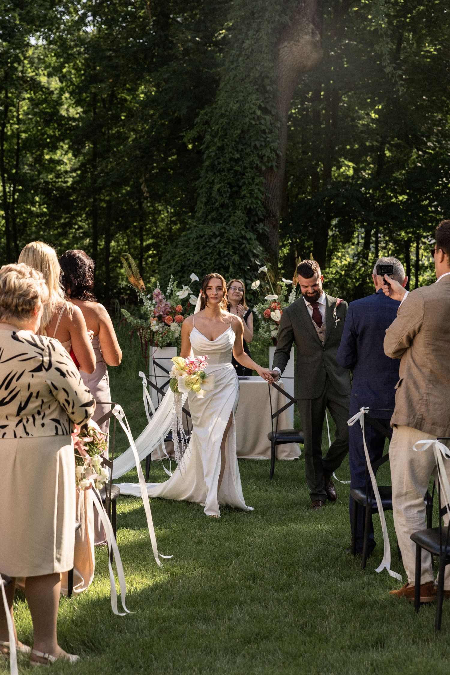Wedding guests and newlyweds celebrating at an outdoor summer ceremony in a lush garden setting.