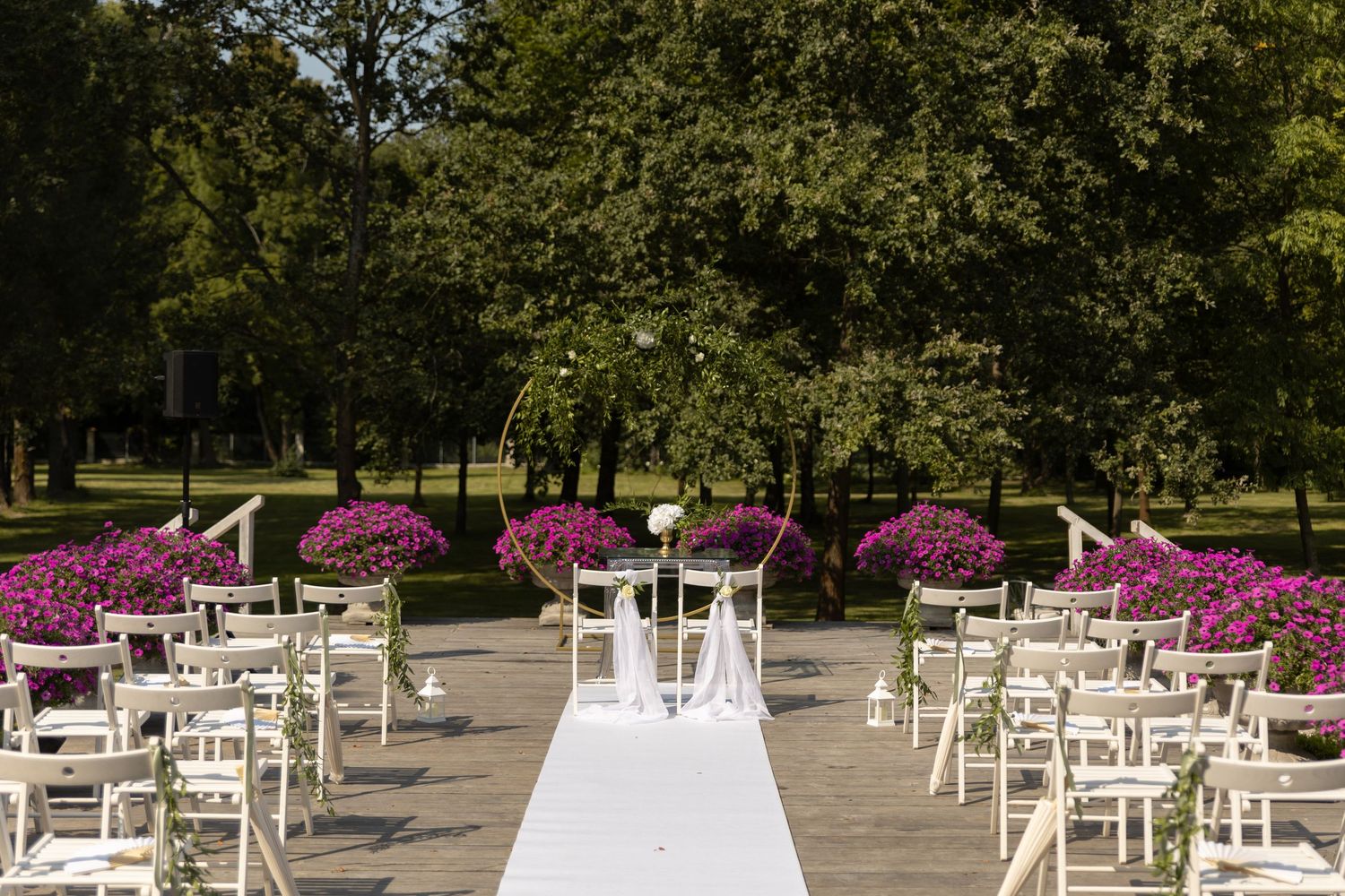 White chairs arranged in rows for an outdoor wedding ceremony with vibrant pink floral decorations and trees in background.