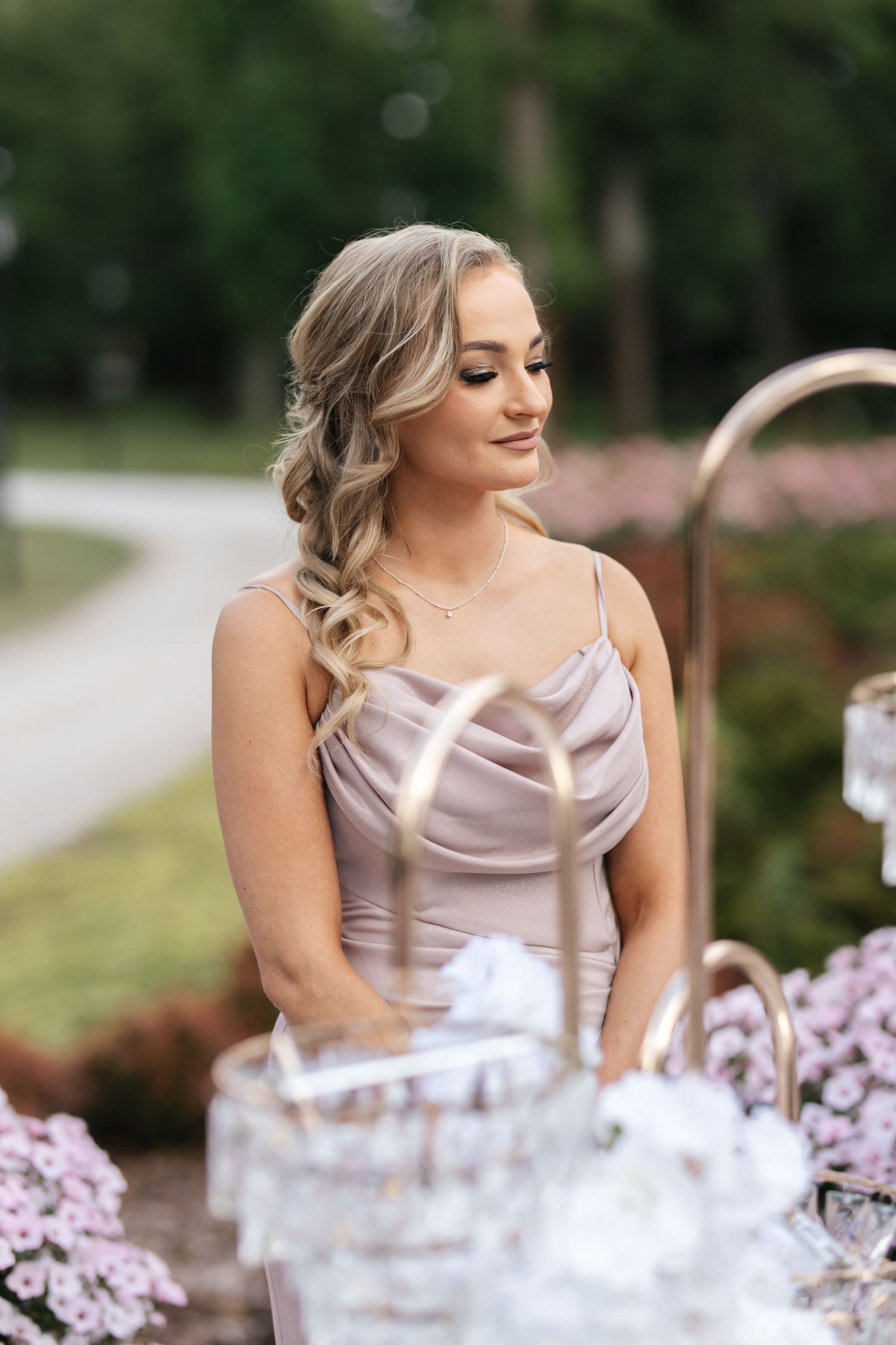 Elegant blonde woman in a satin slip dress standing outdoors at a garden event with floral decorations.
