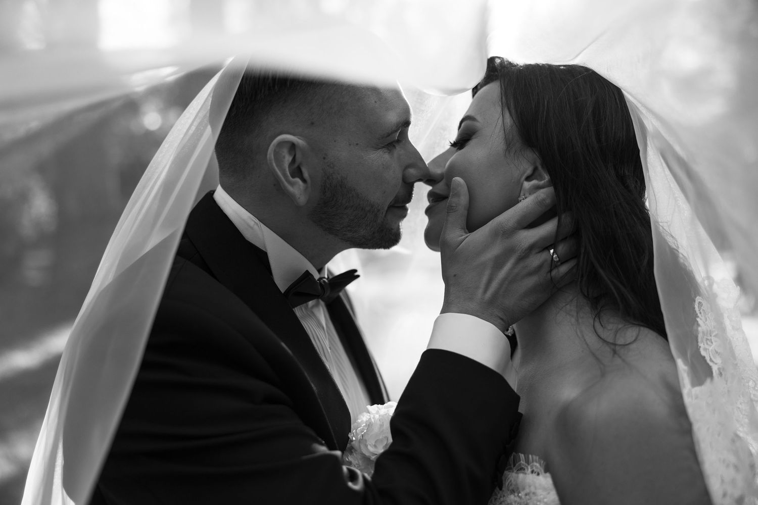 Black and white wedding photo of bride and groom sharing an intimate moment under a veil.
