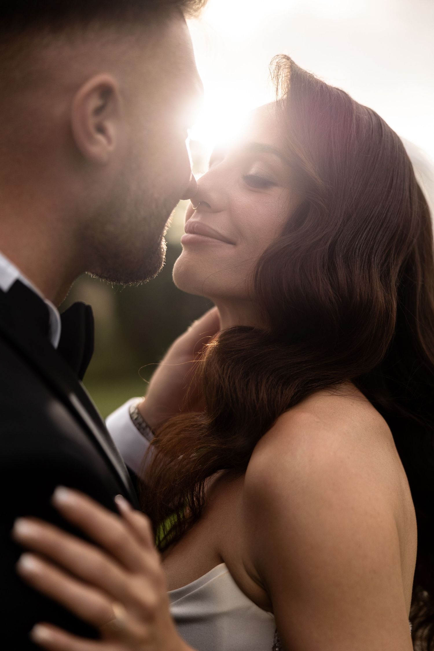A bride and groom share an intimate moment, bathed in warm golden sunlight, as they lean close together.