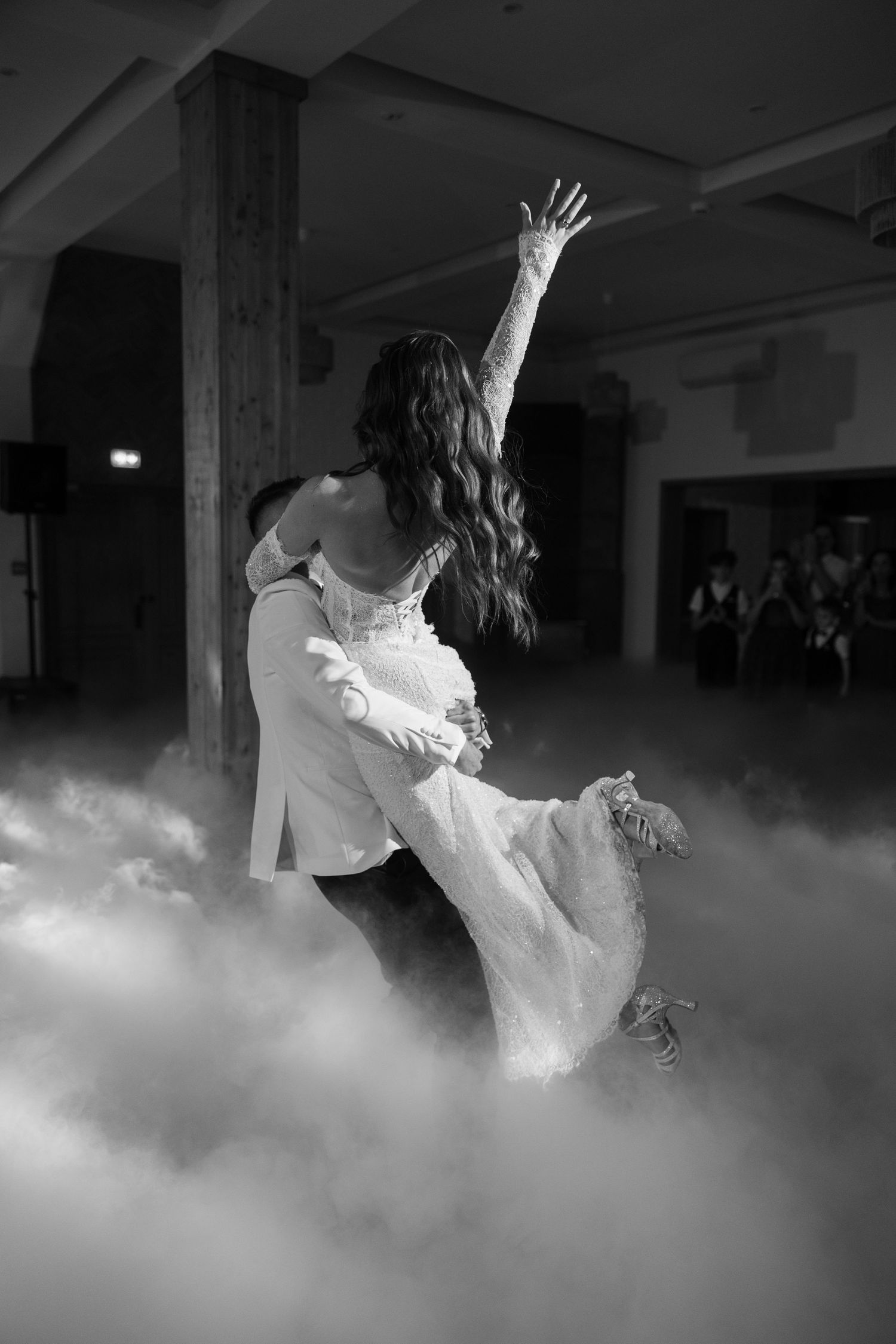 Black and white photo of bride and groom sharing first dance surrounded by dramatic fog at wedding reception.