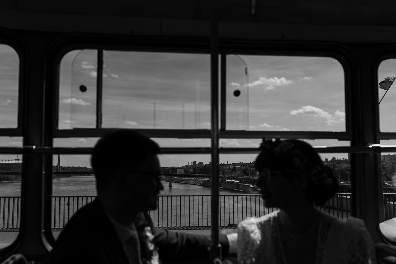 Two silhouetted figures sit by a window on a train or ferry, with water and sky visible through the glass.