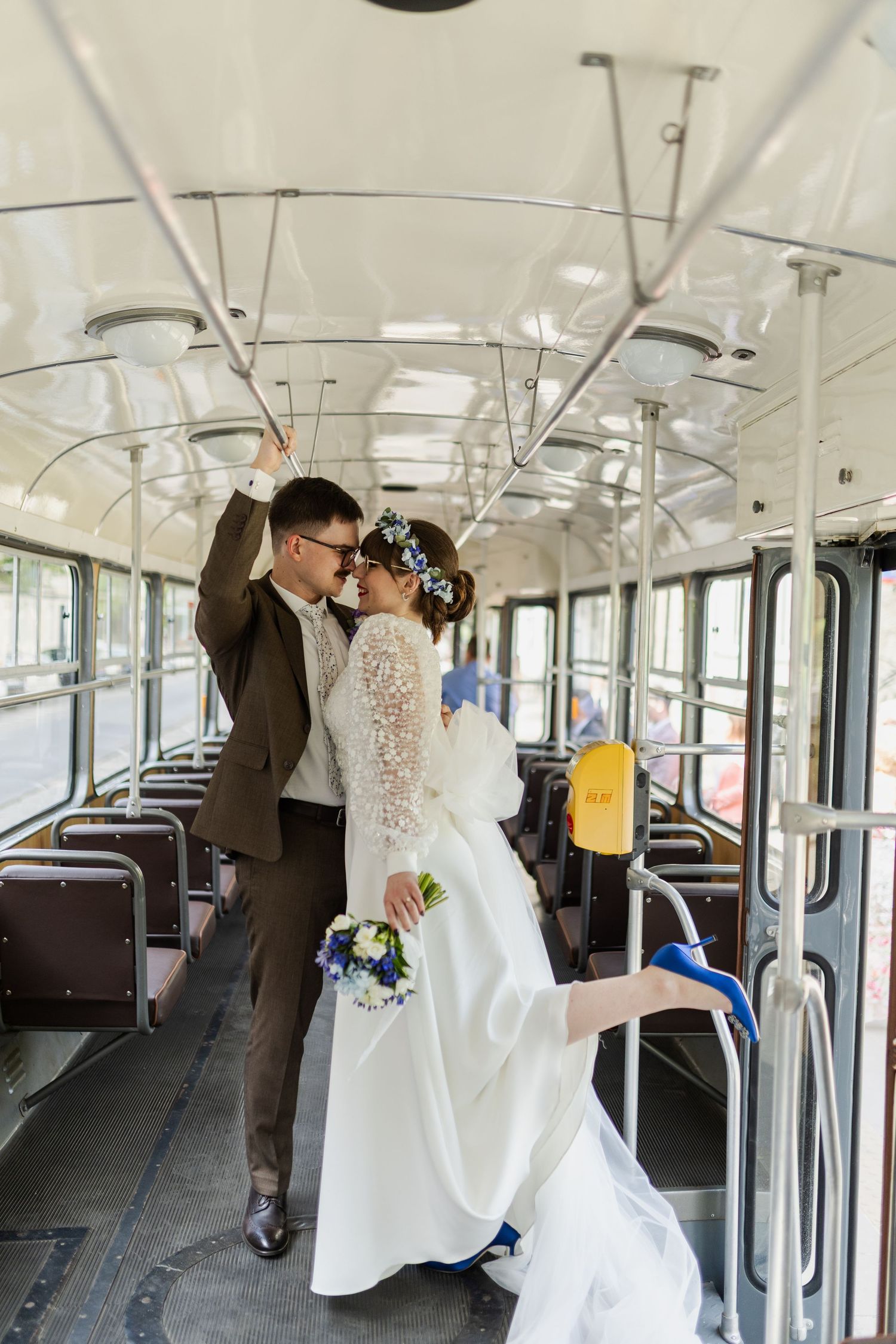 Couple in wedding attire holding onto railings inside a vintage public transit bus with a rustic interior.