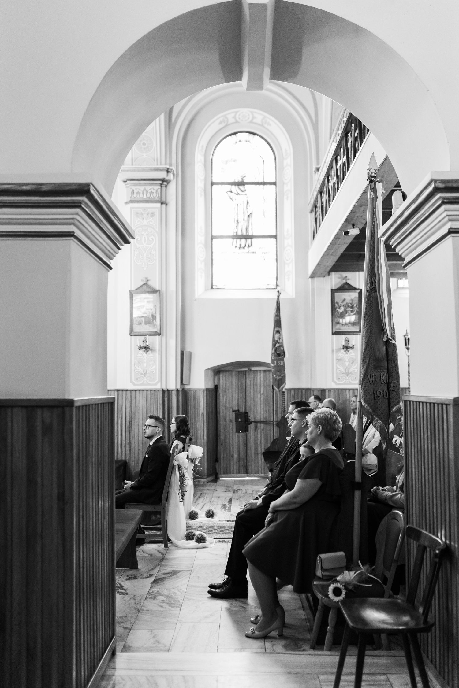 A black and white interior photo of people sitting in church pews under an arched ceiling with ornate woodwork.