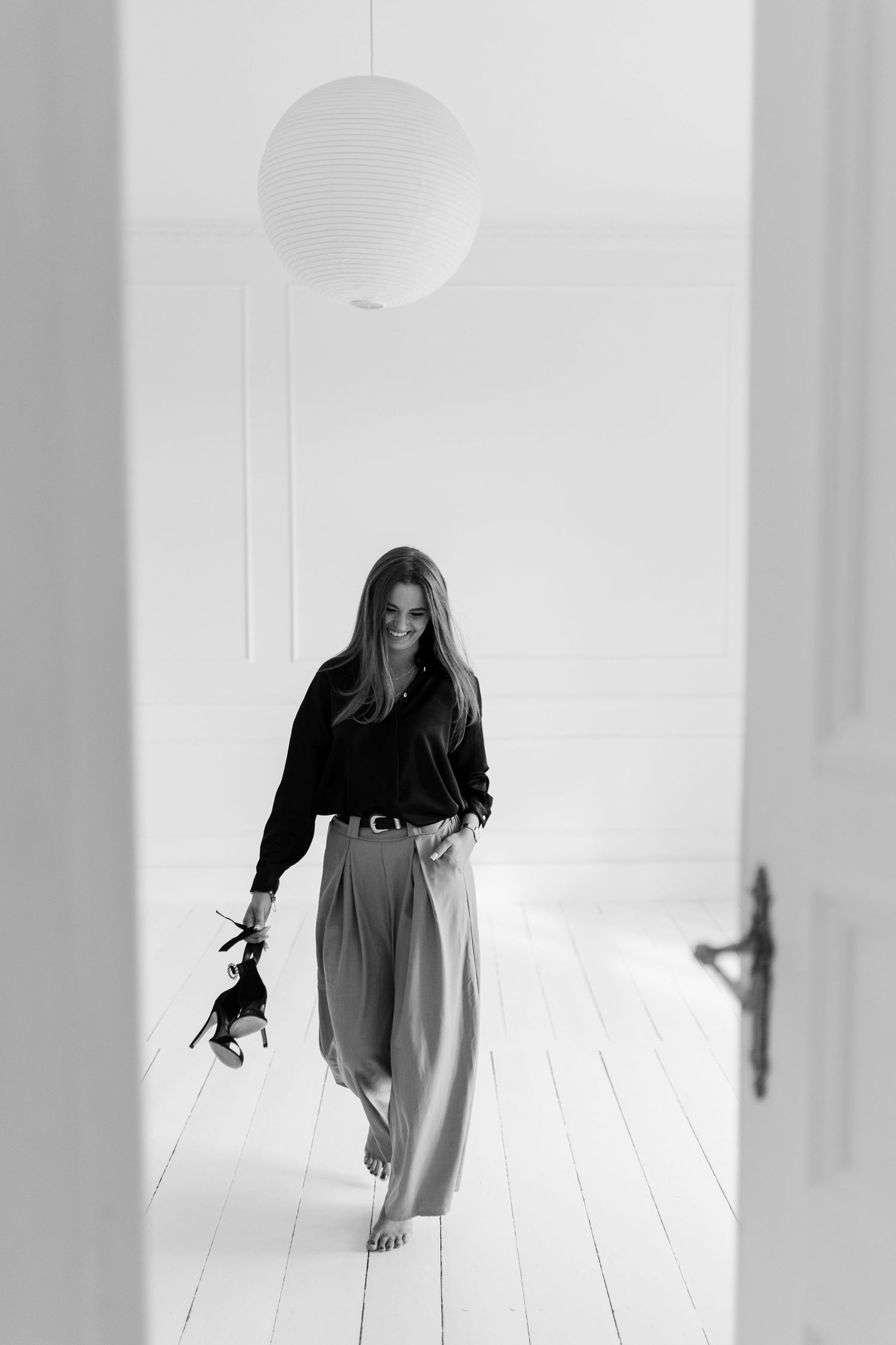 Black and white photo of figure in flowing outfit walking gracefully through bright minimalist interior.