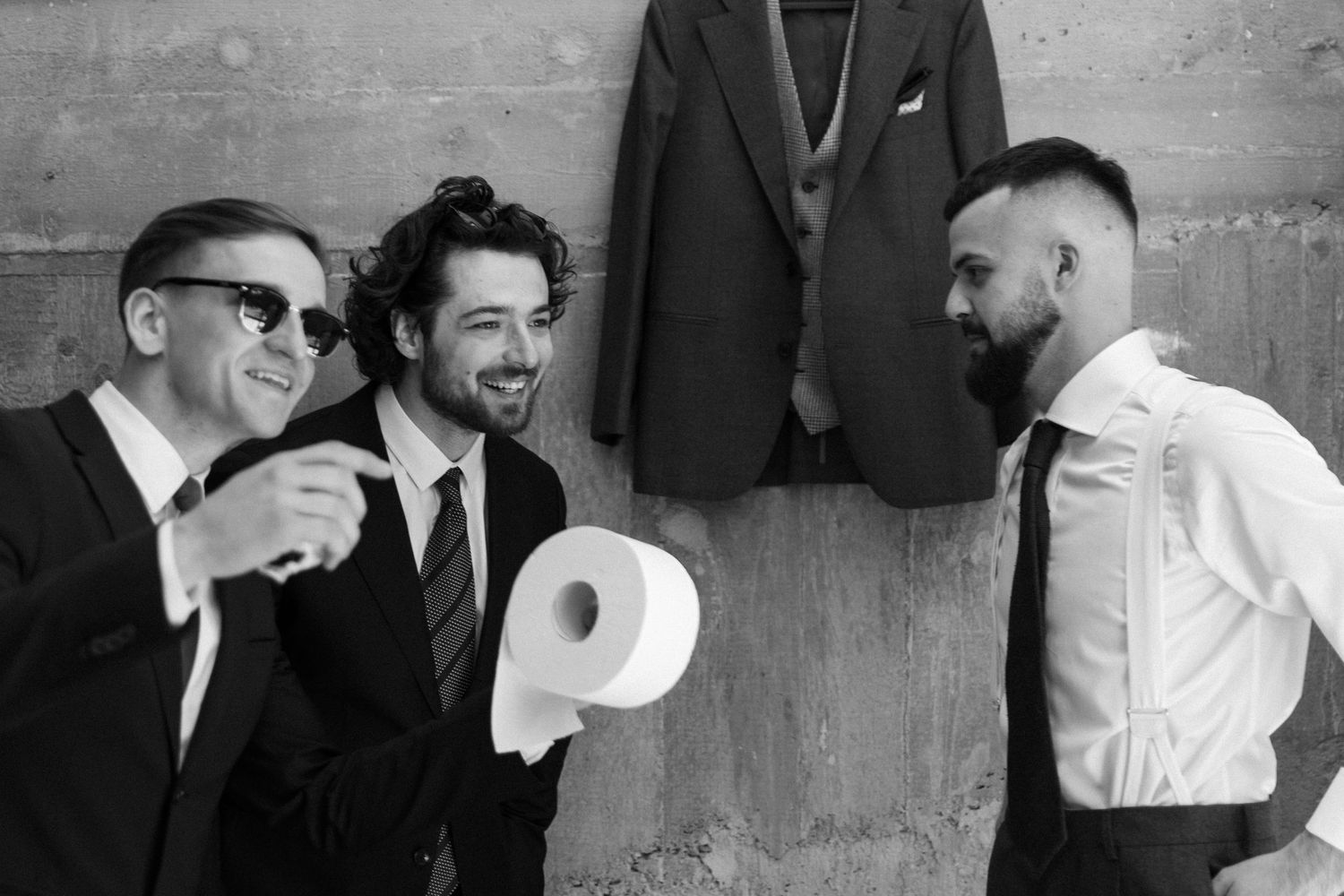 Three men in formal attire share a laugh around a megaphone in a black and white photograph.
