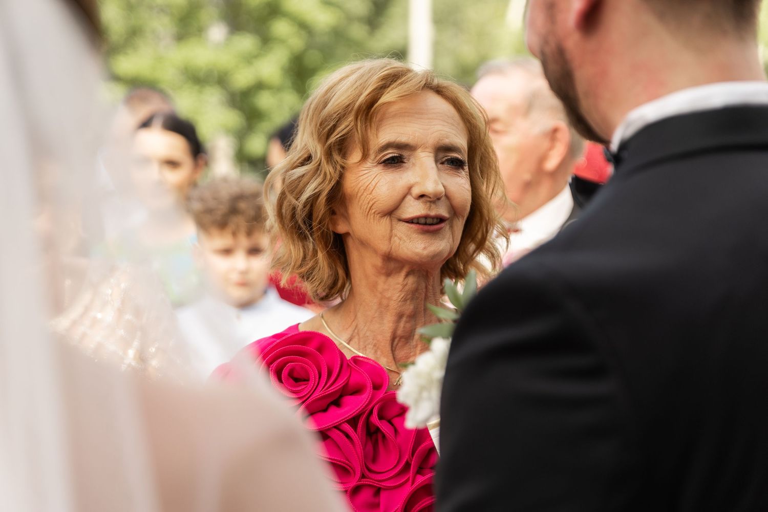 A wedding celebration outdoors with bright pink rose bouquets and formal attire against a natural backdrop.