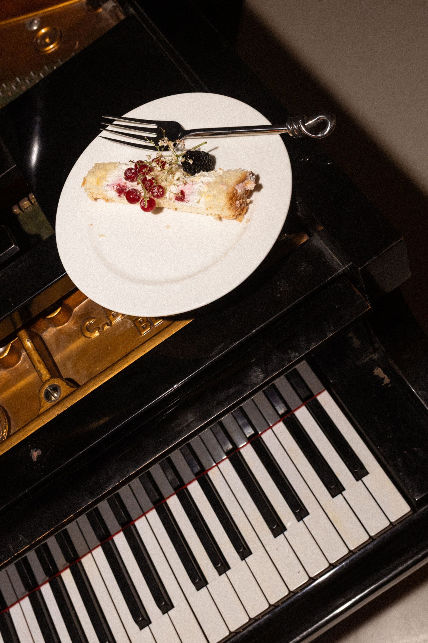 A half-eaten dessert plate rests on top of a black piano keyboard in an artistic composition.