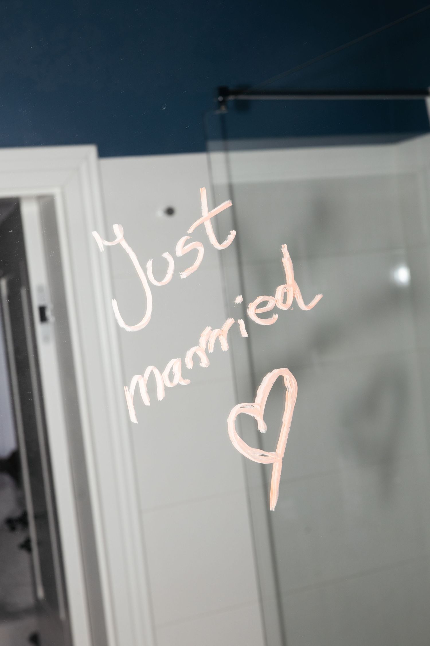 Just married written with a heart on a glass shower door in a modern bathroom with blue walls.