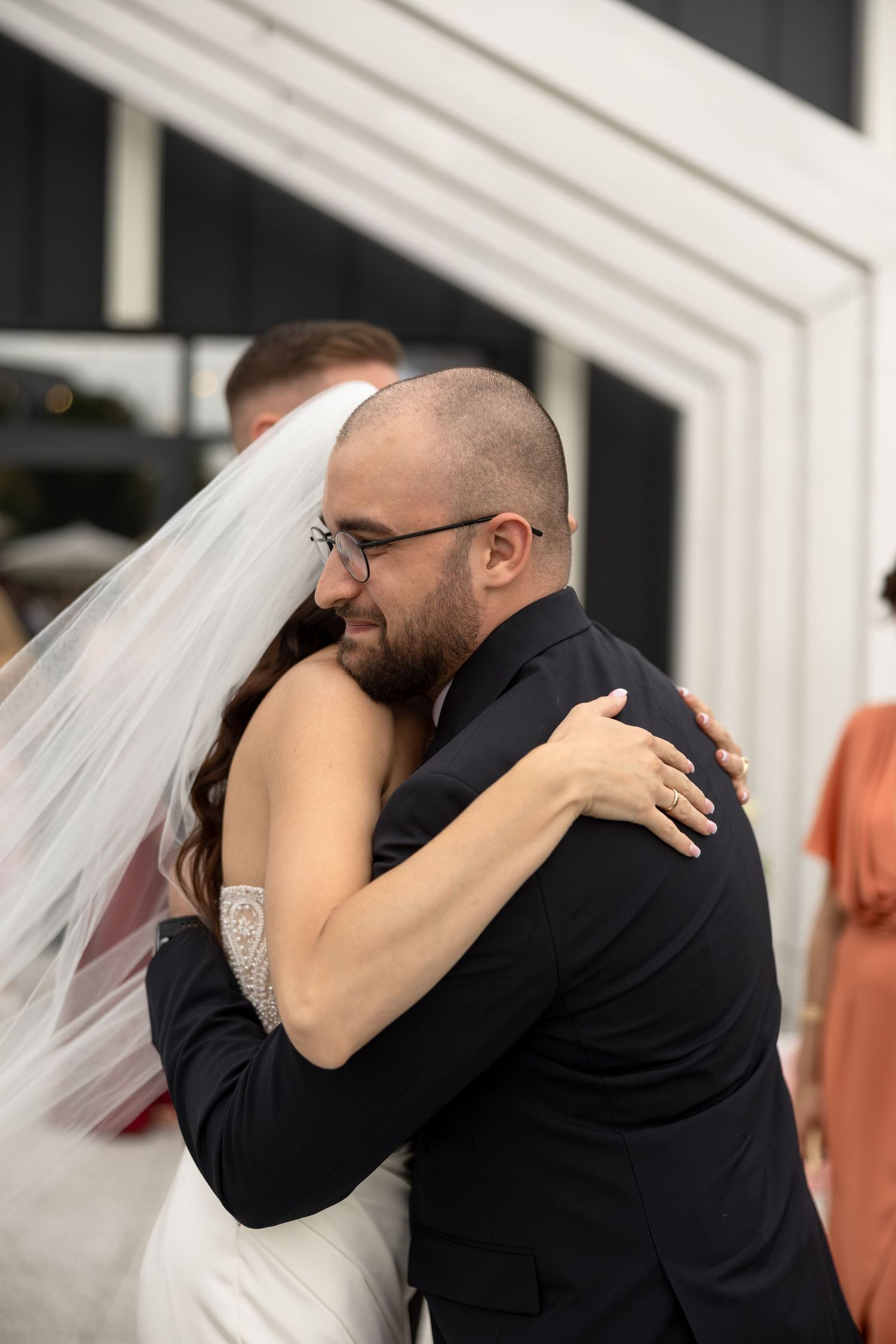 Bride and groom share an emotional first hug during their wedding ceremony, bride wearing veil and white gown.