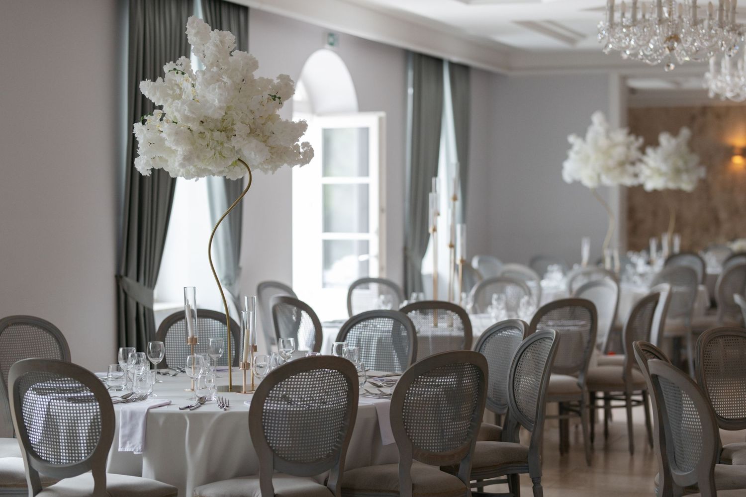Elegant wedding reception hall with white floral centerpieces, gray chairs, and chandelier lighting.